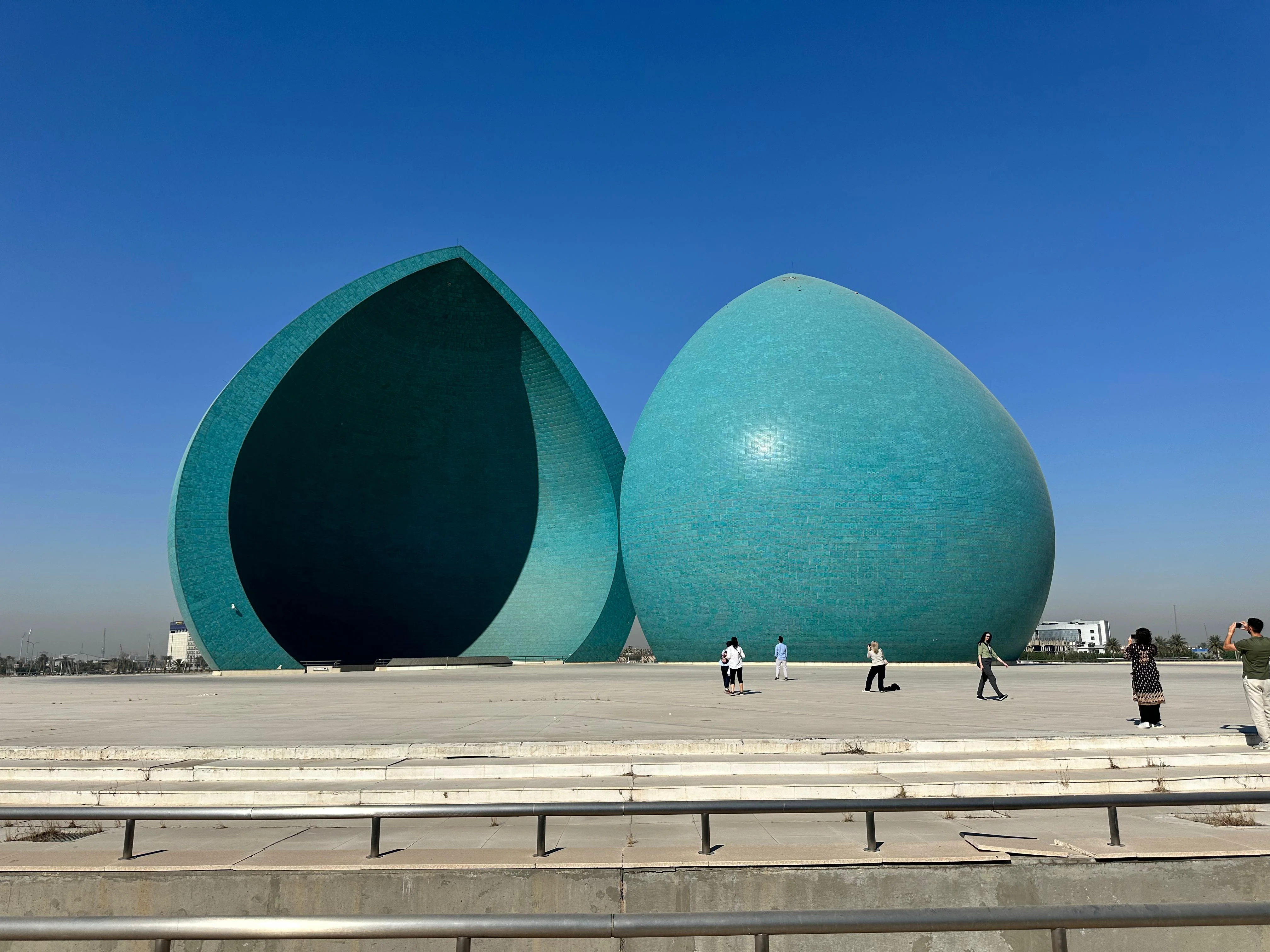 Martyrs Monument in Baghdad, Iraq with teal domes under a bright blue sky and tourists around
