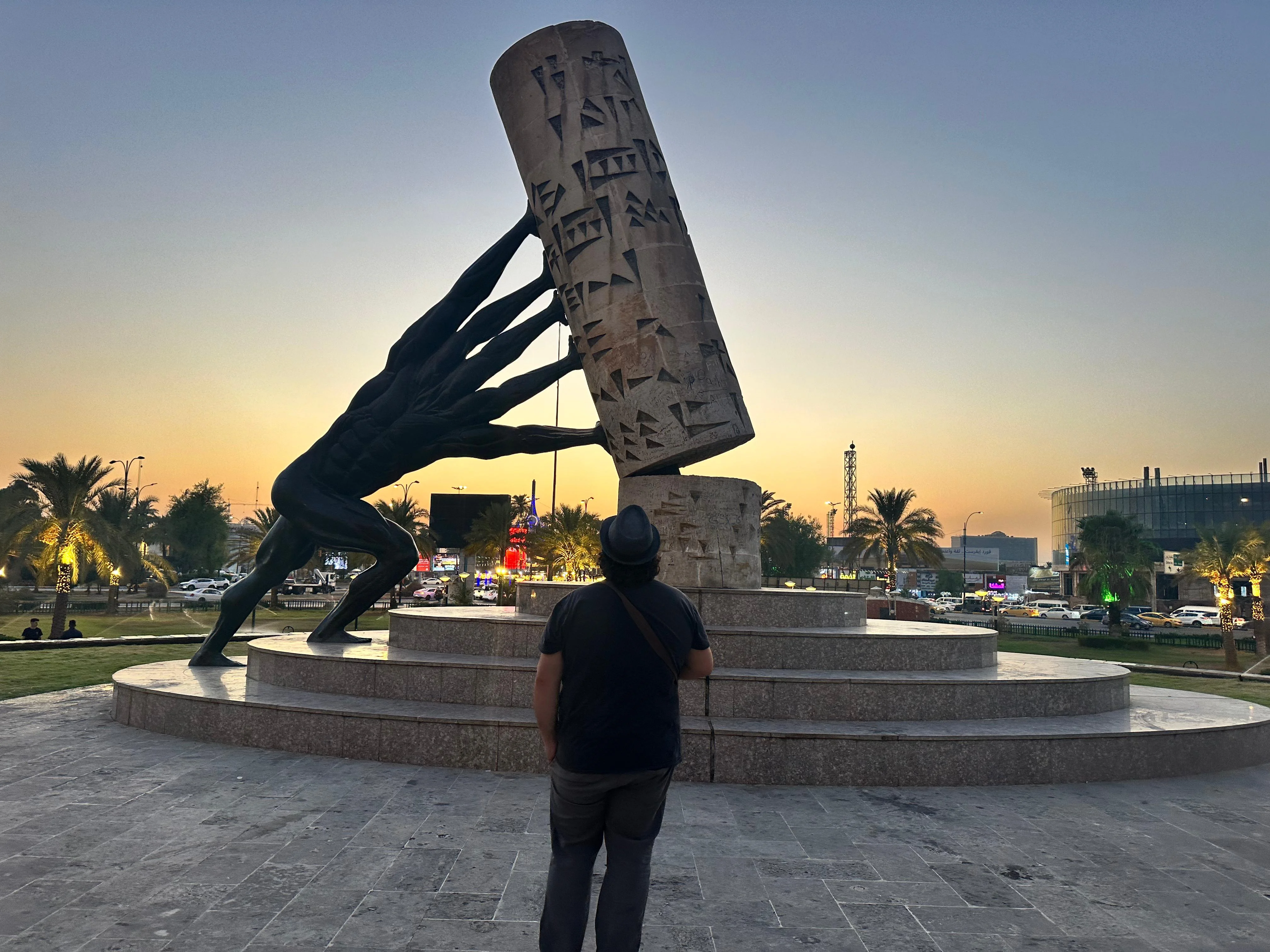 Monument of Strength statue in Iraq with a man observing at sunset, modern city in background