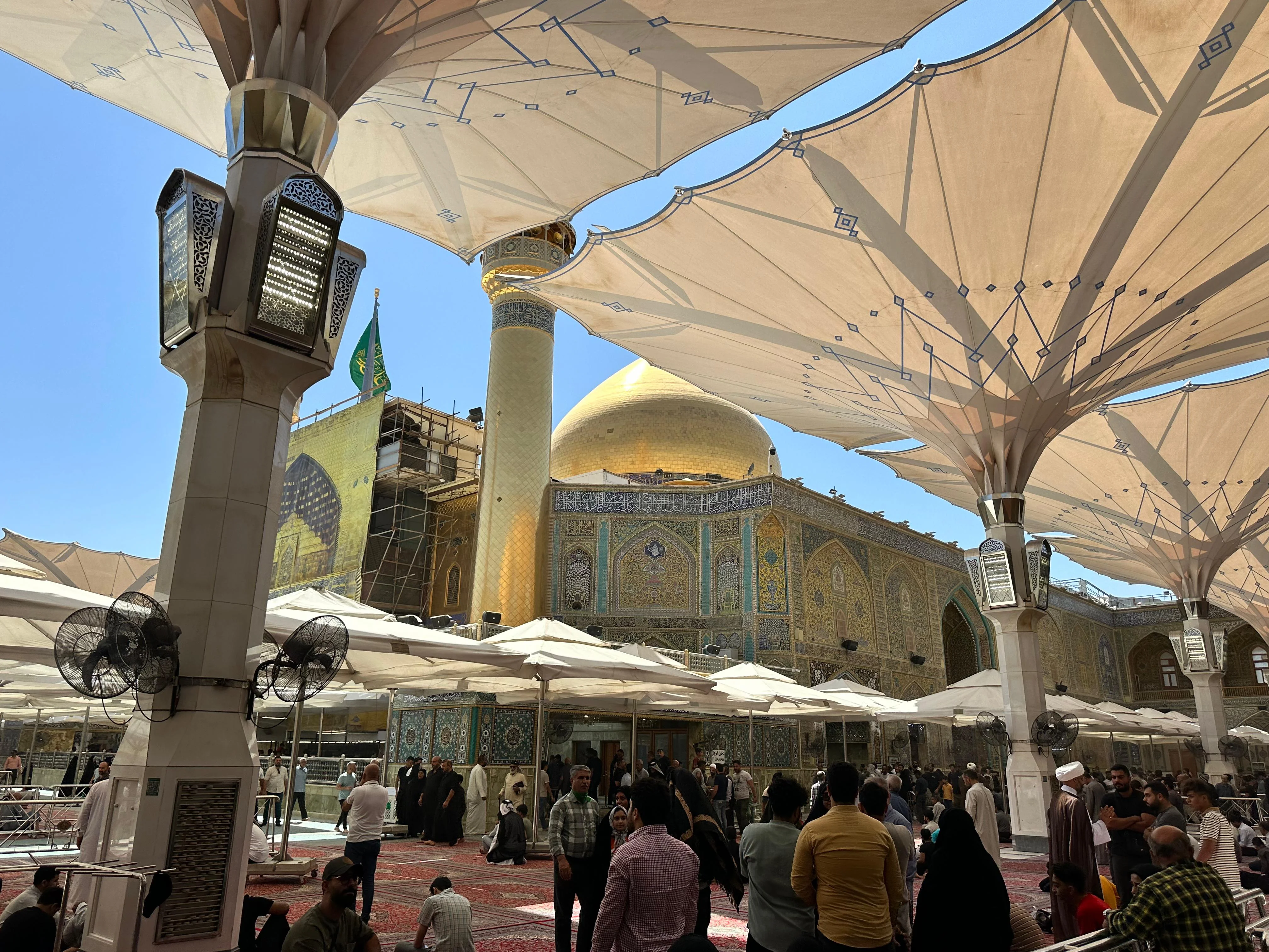 Golden dome and minarets of Imam Ali Shrine in Najaf, Iraq with worshippers in the shaded courtyard
