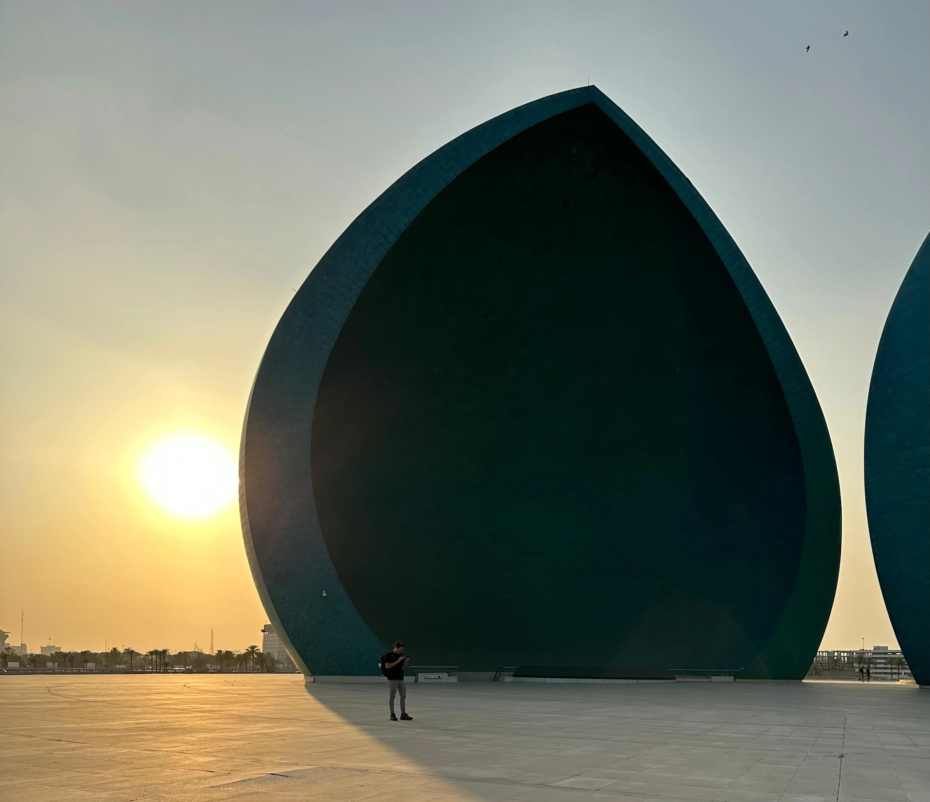 Martyrs Monument in Baghdad, Iraq at sunset, with a person standing near the large teal domes
