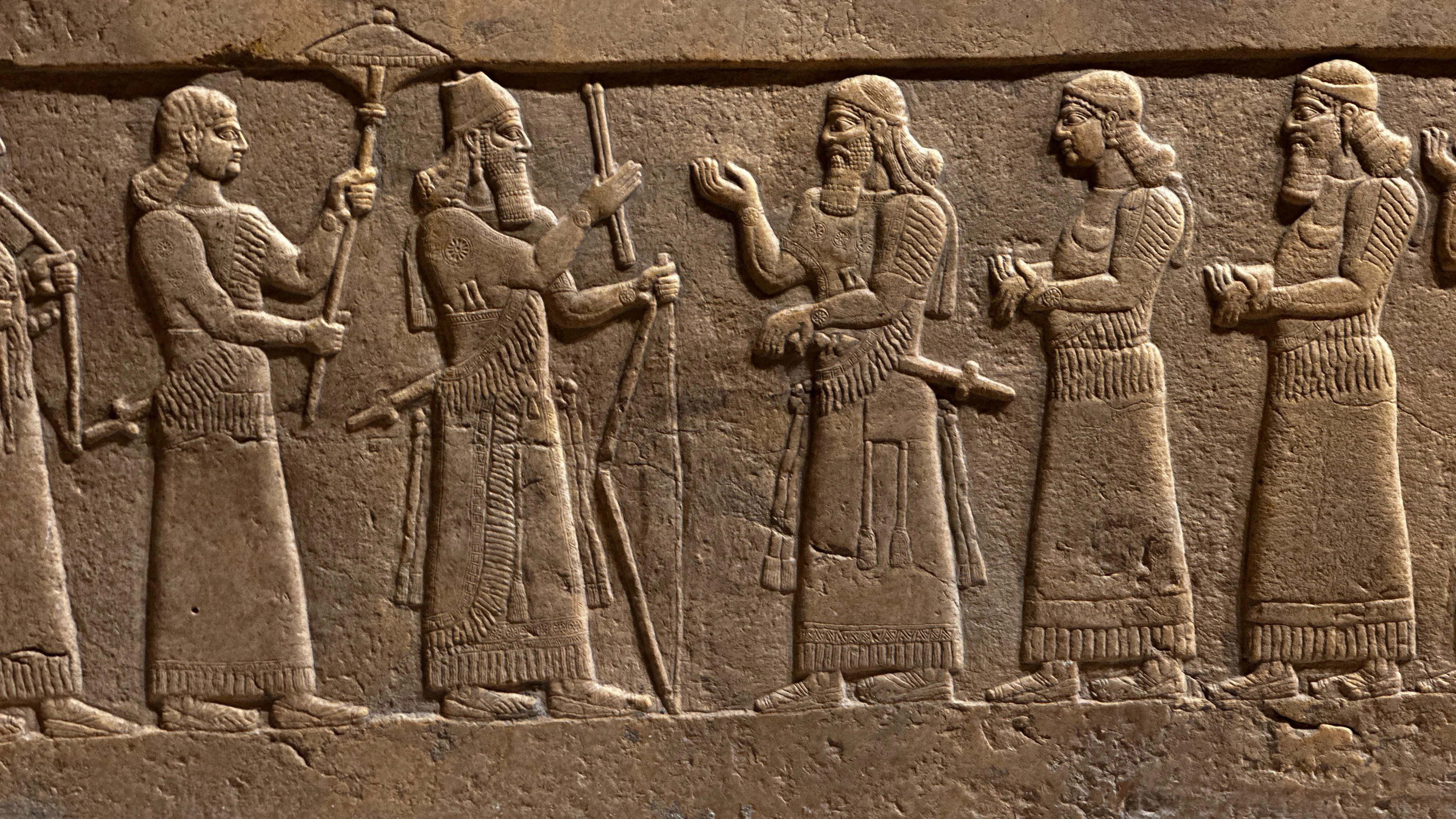 Assyrian stone relief showing royal figures in profile, carved with fine detail from ancient Mesopotamia