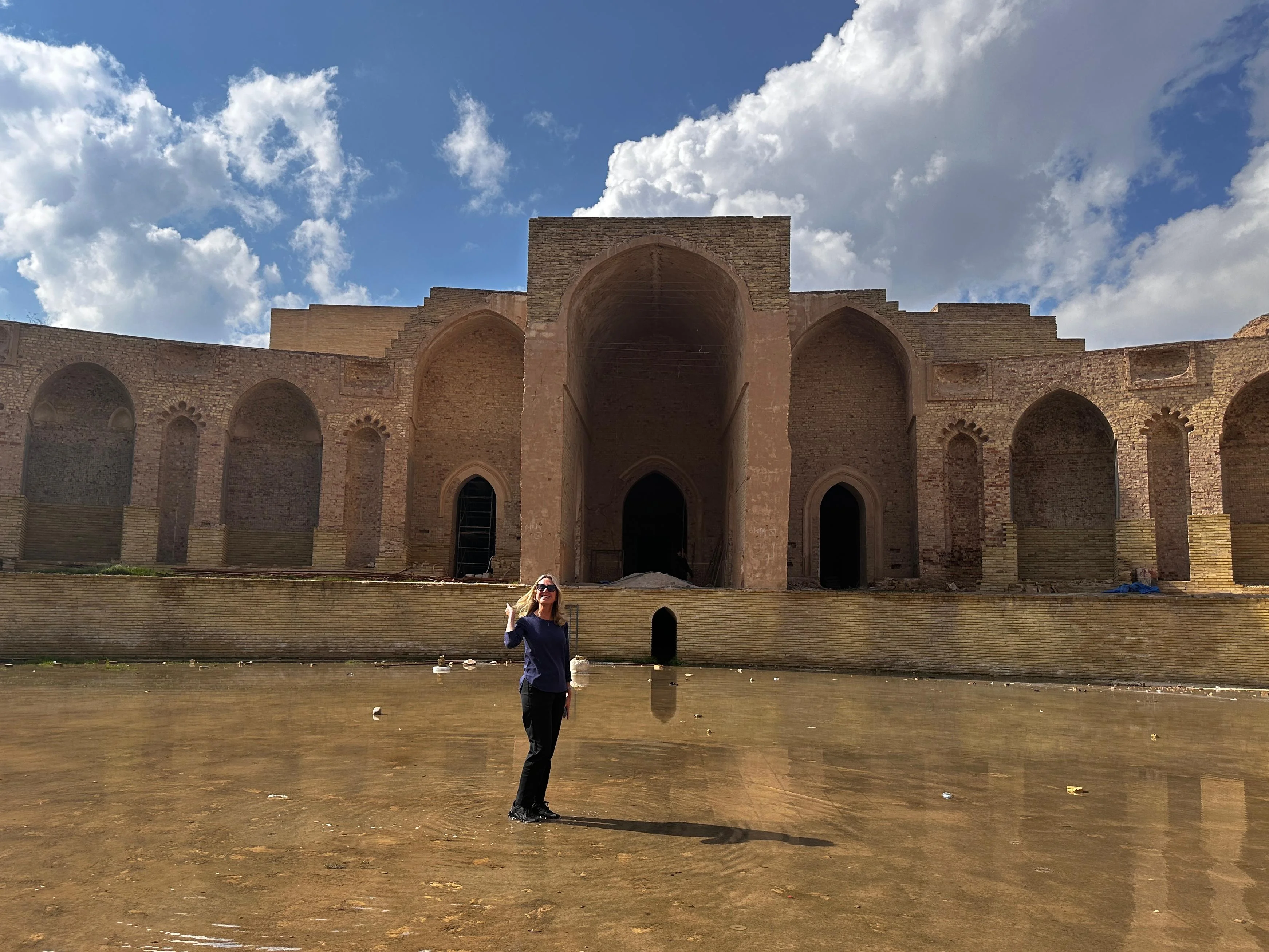 Woman standing in front of the Great Mosque of Samarra in Iraq, reflected in shallow water