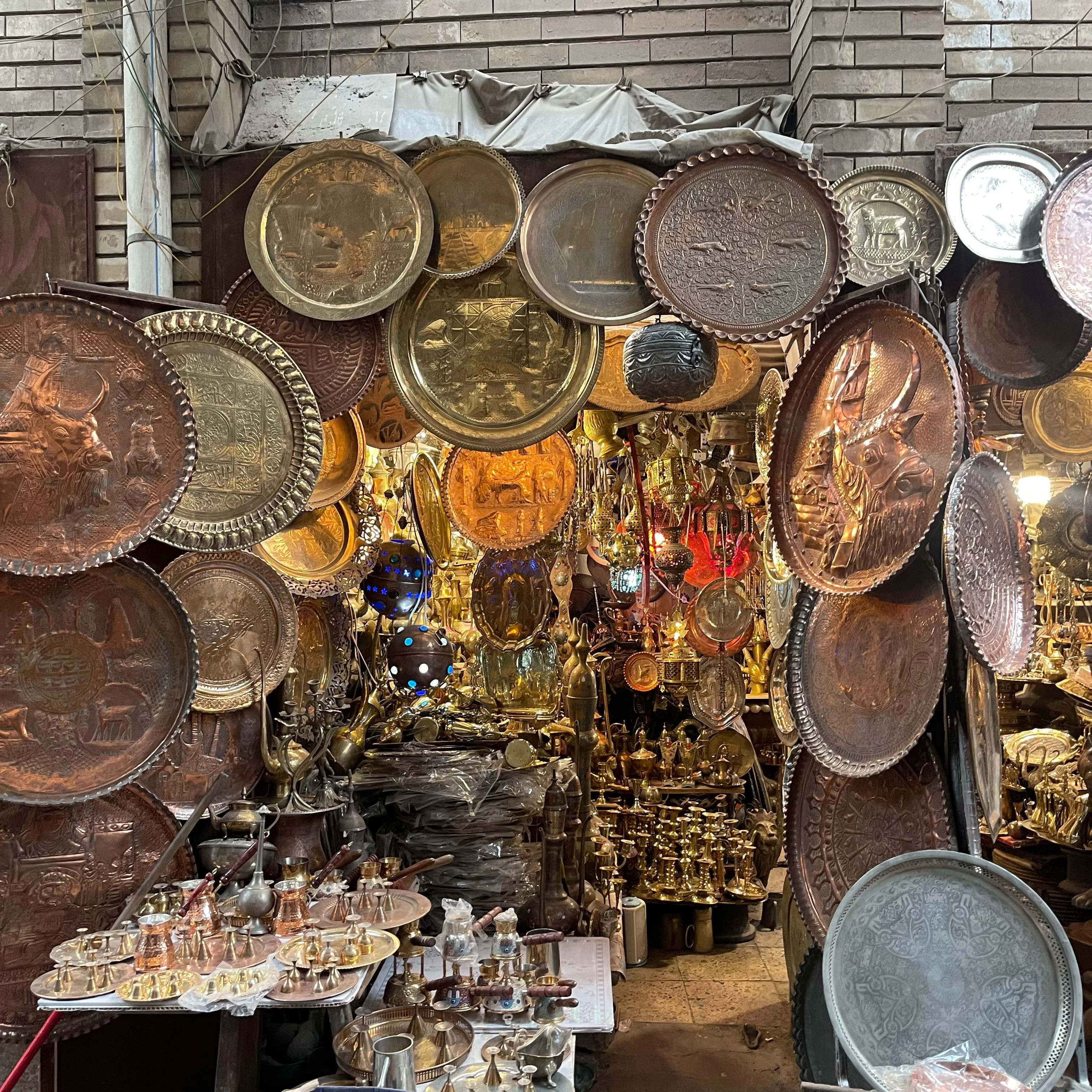 Copper and brass plates hanging in a traditional Iraqi market filled with antique lamps and teapots