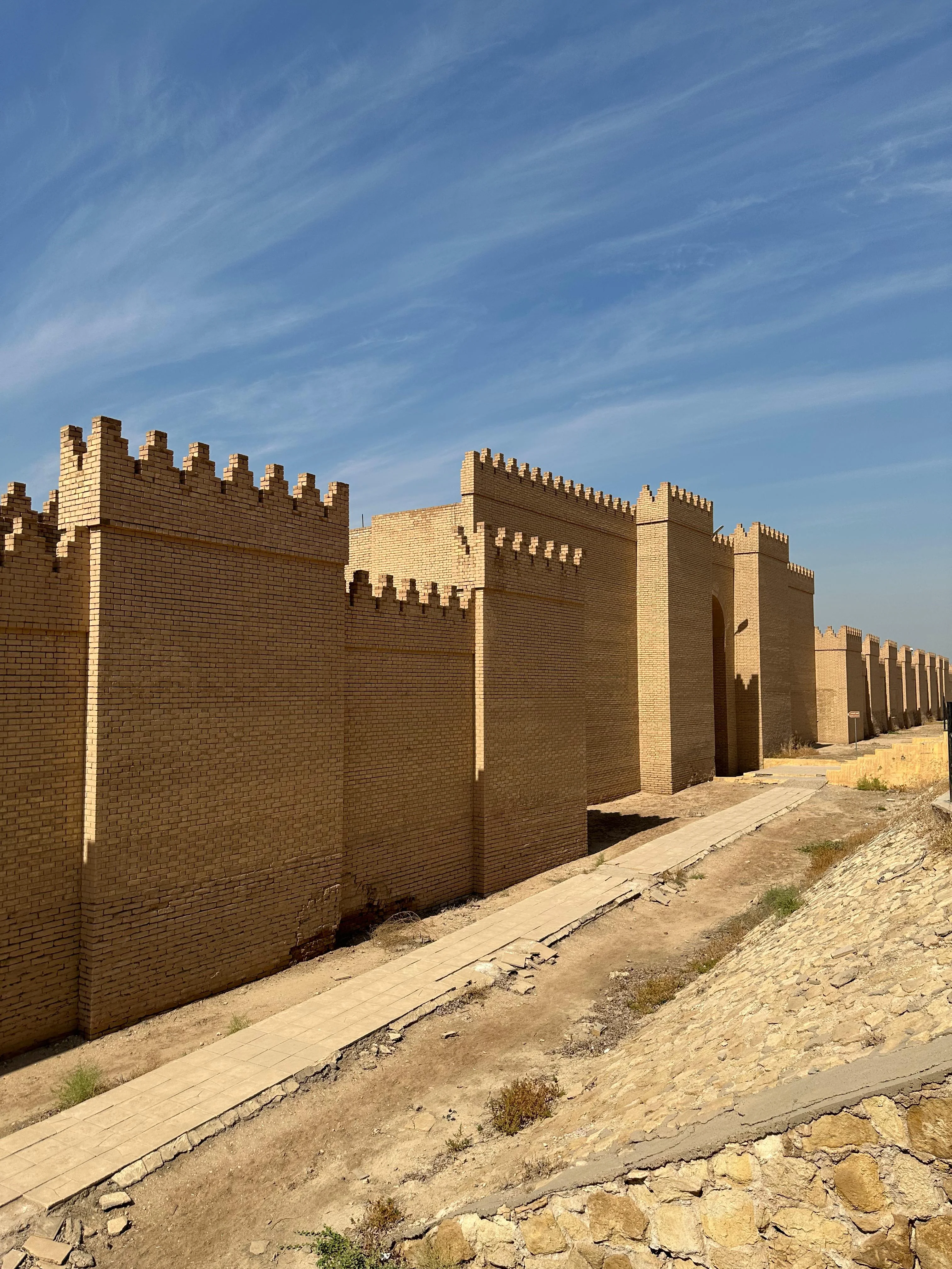 View of ancient Babylon’s fortified walls in Iraq under a blue sky, showcasing restored brickwork