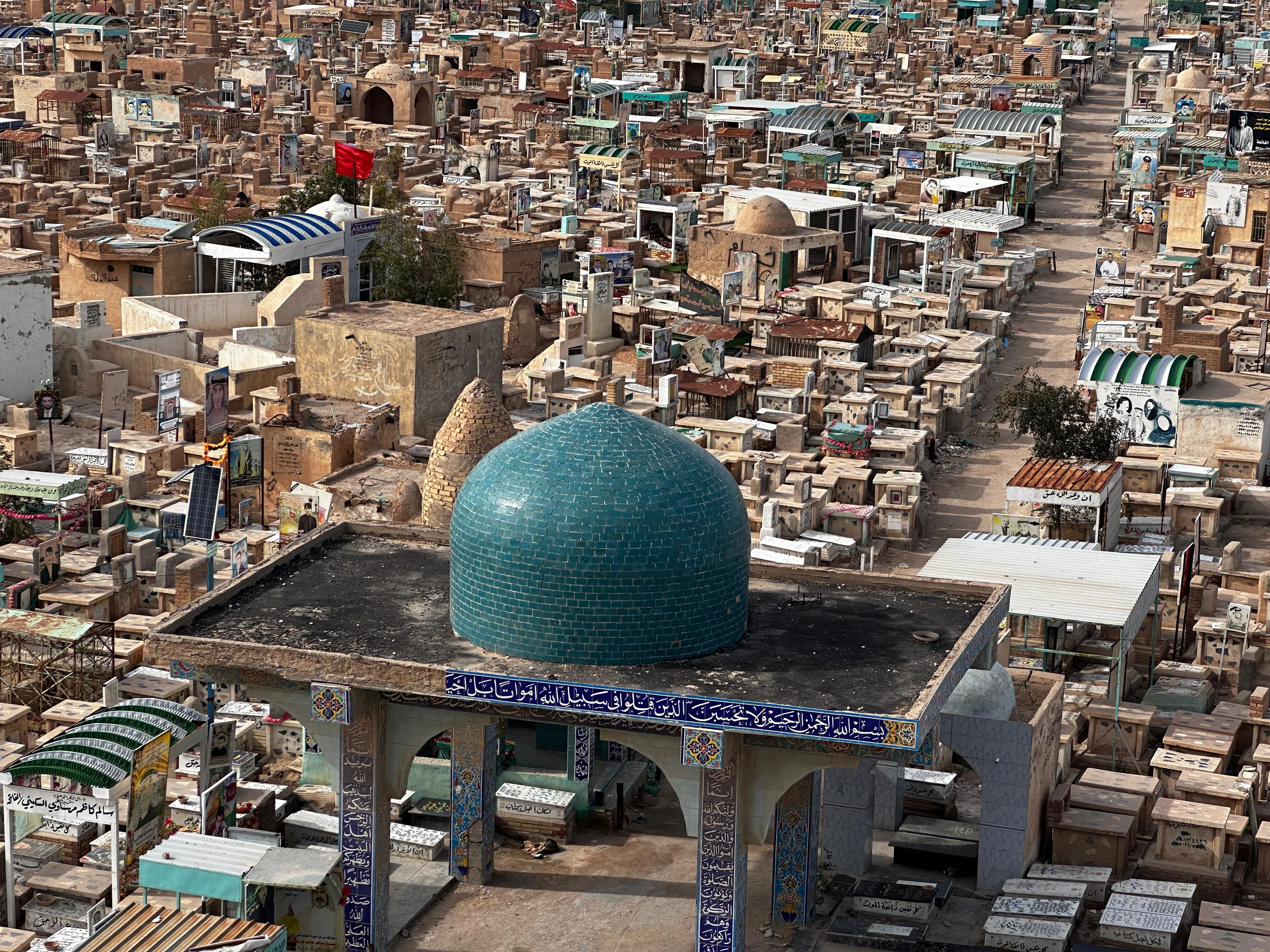 Aerial view of Wadi Al-Salam cemetery in Najaf, Iraq, with turquoise dome and dense tomb structures.