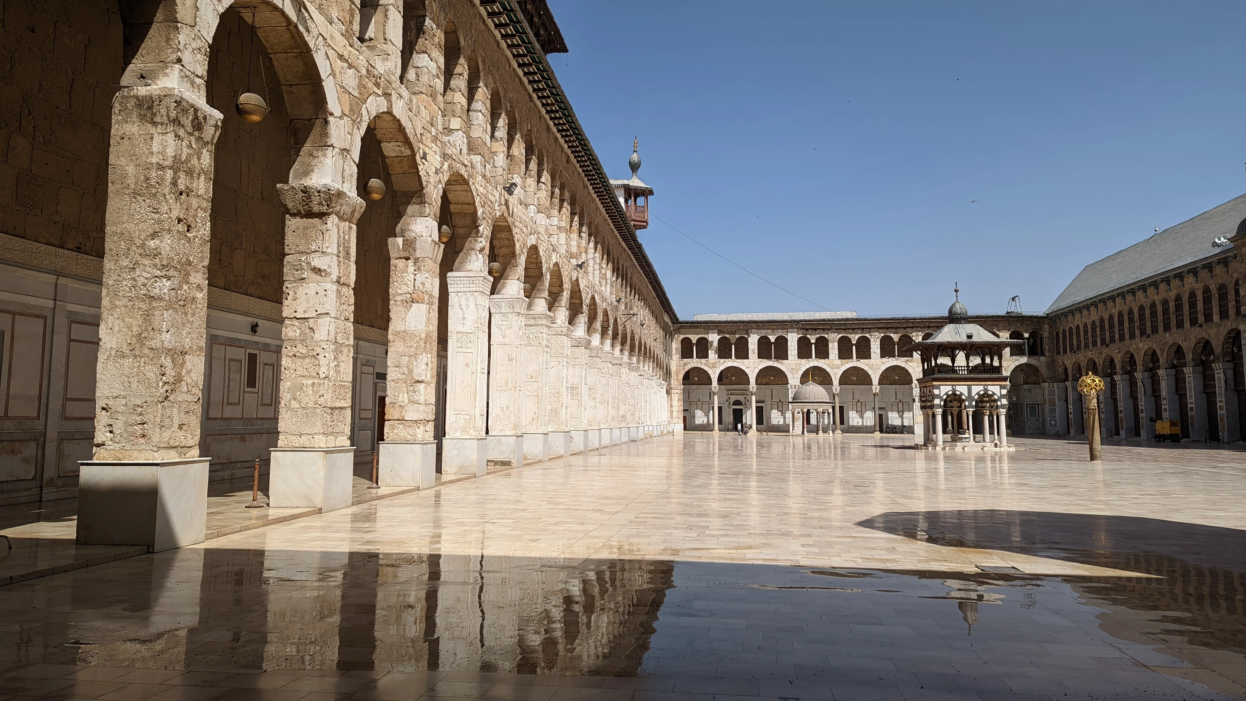Side view of Umayyad Mosque courtyard showing stone arches and water reflections on marble floor