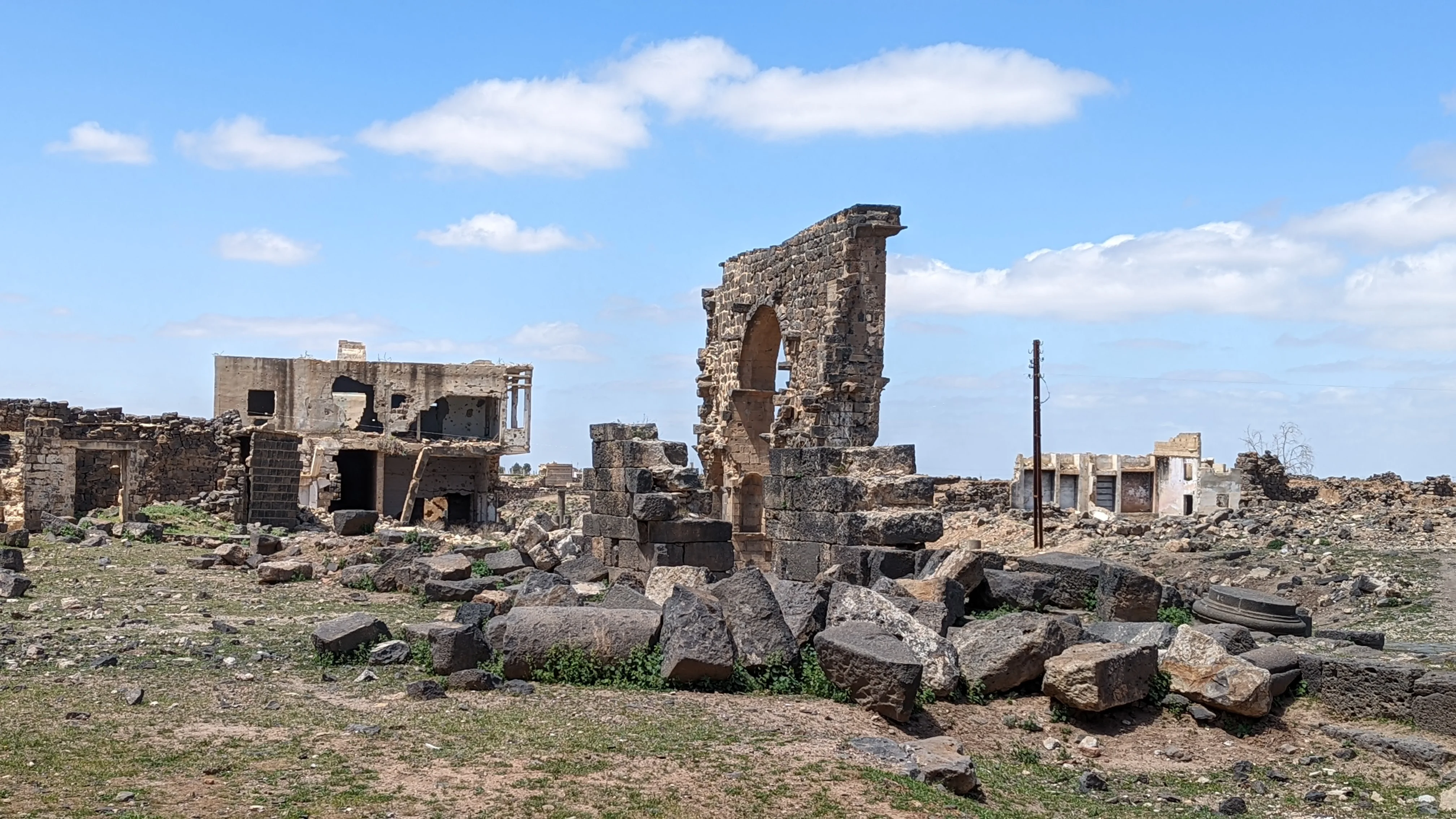 Ruins of damaged stone buildings and archways in an abandoned Syrian village under blue sky