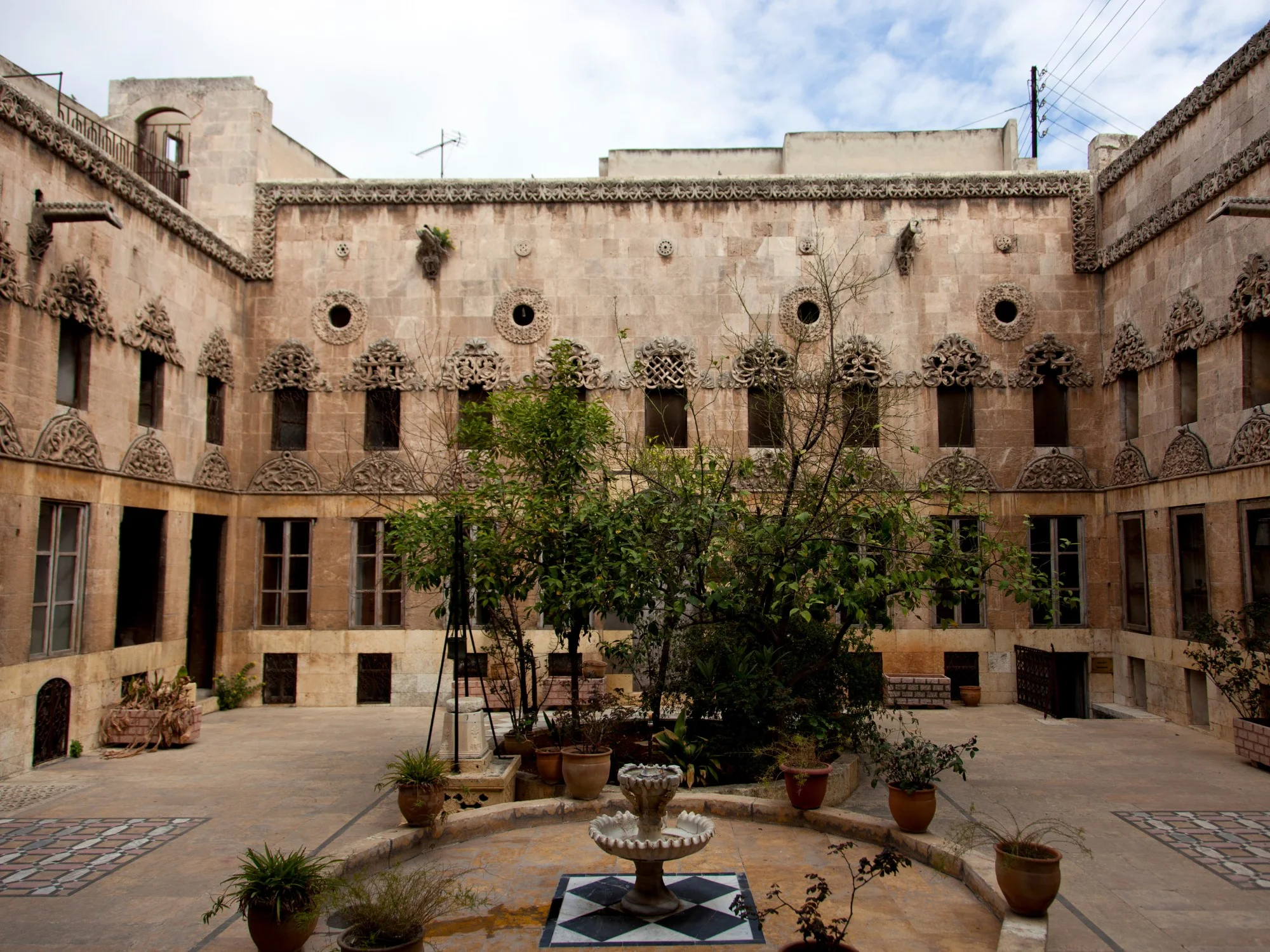 Traditional courtyard in Aleppo's Al-Mihmandar House with carved stone windows and central fountain