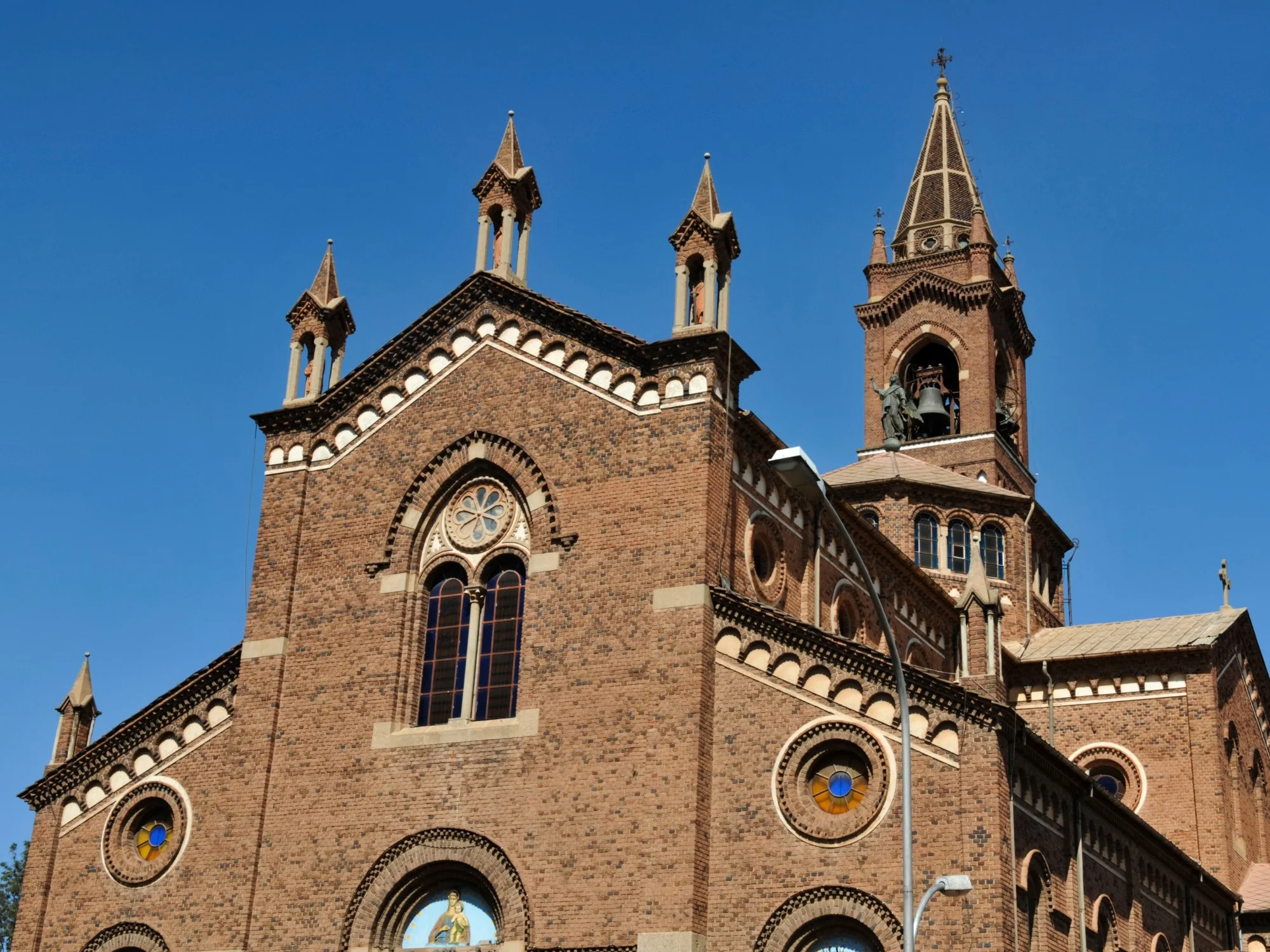 Front facade of Asmara’s red-brick Catholic Cathedral with rose windows, spires and bell tower under a clear blue sky