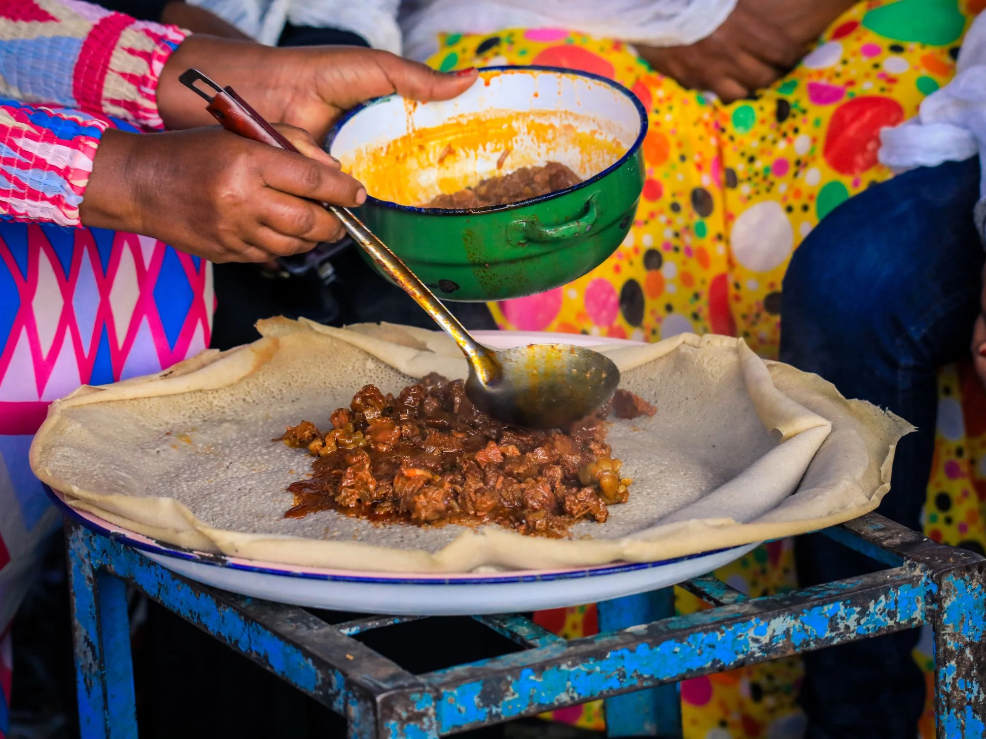 Traditional Eritrean meal: person serving spicy stew onto large injera flatbread on a platter during communal dining
