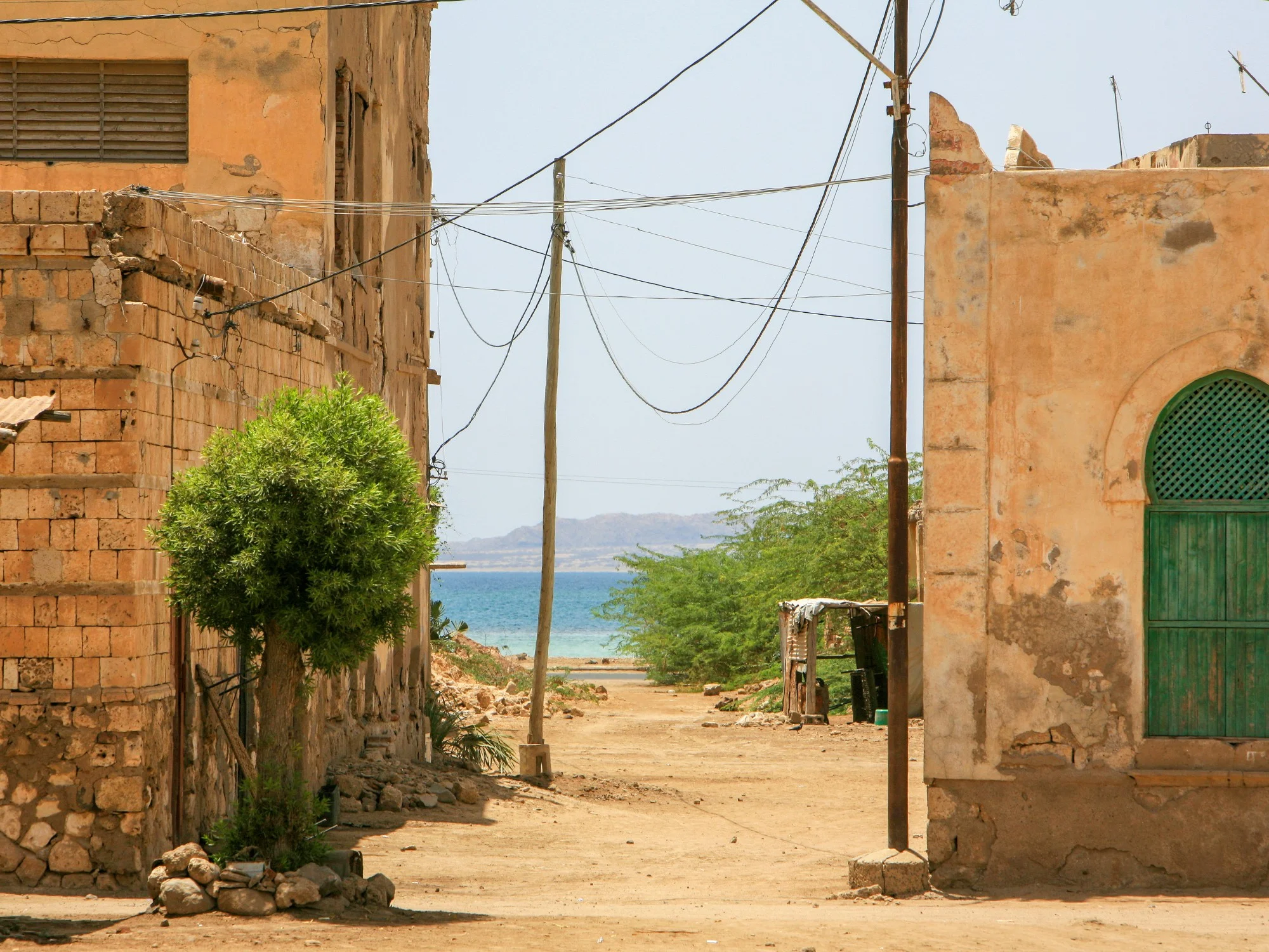 Dusty alley in Massawa, Eritrea with coral-stone houses, green wooden door, overhead wires and Red Sea glimpse