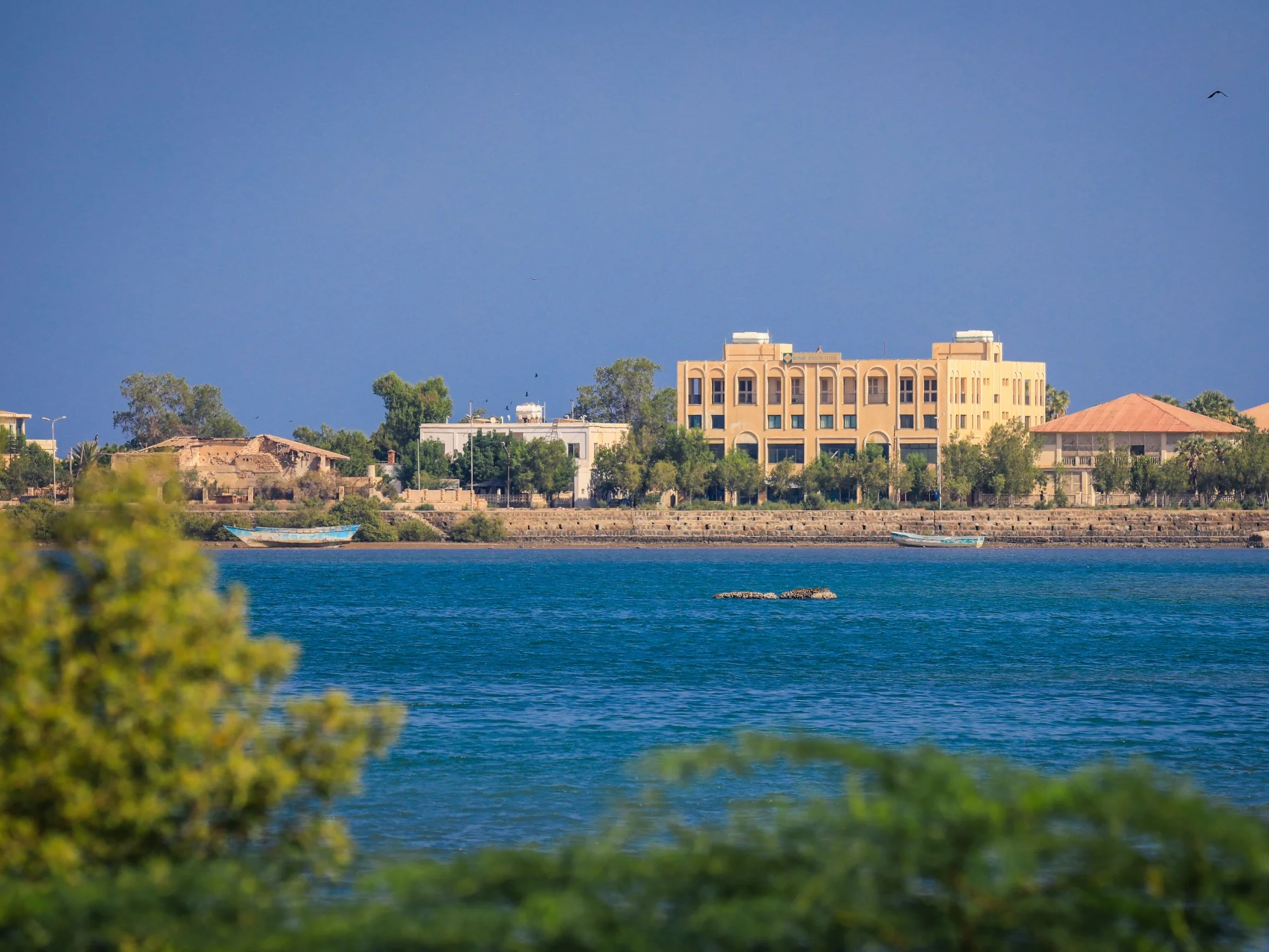 View across turquoise Massawa harbor toward colonial-era buildings and palm trees lining the Eritrean shoreline