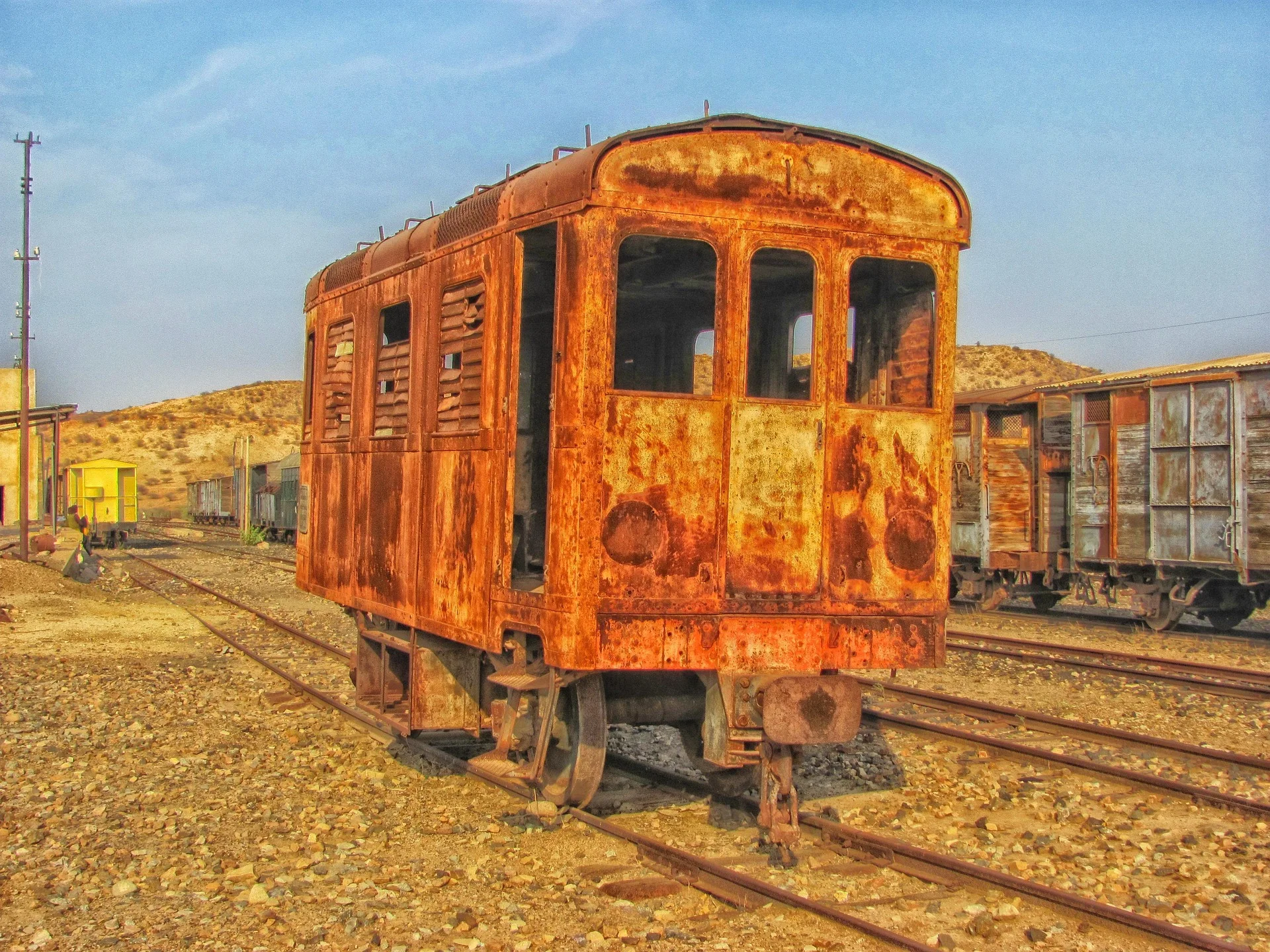 Rusty vintage carriage on Eritrea's old railway with desert hills and weathered freight cars in the background