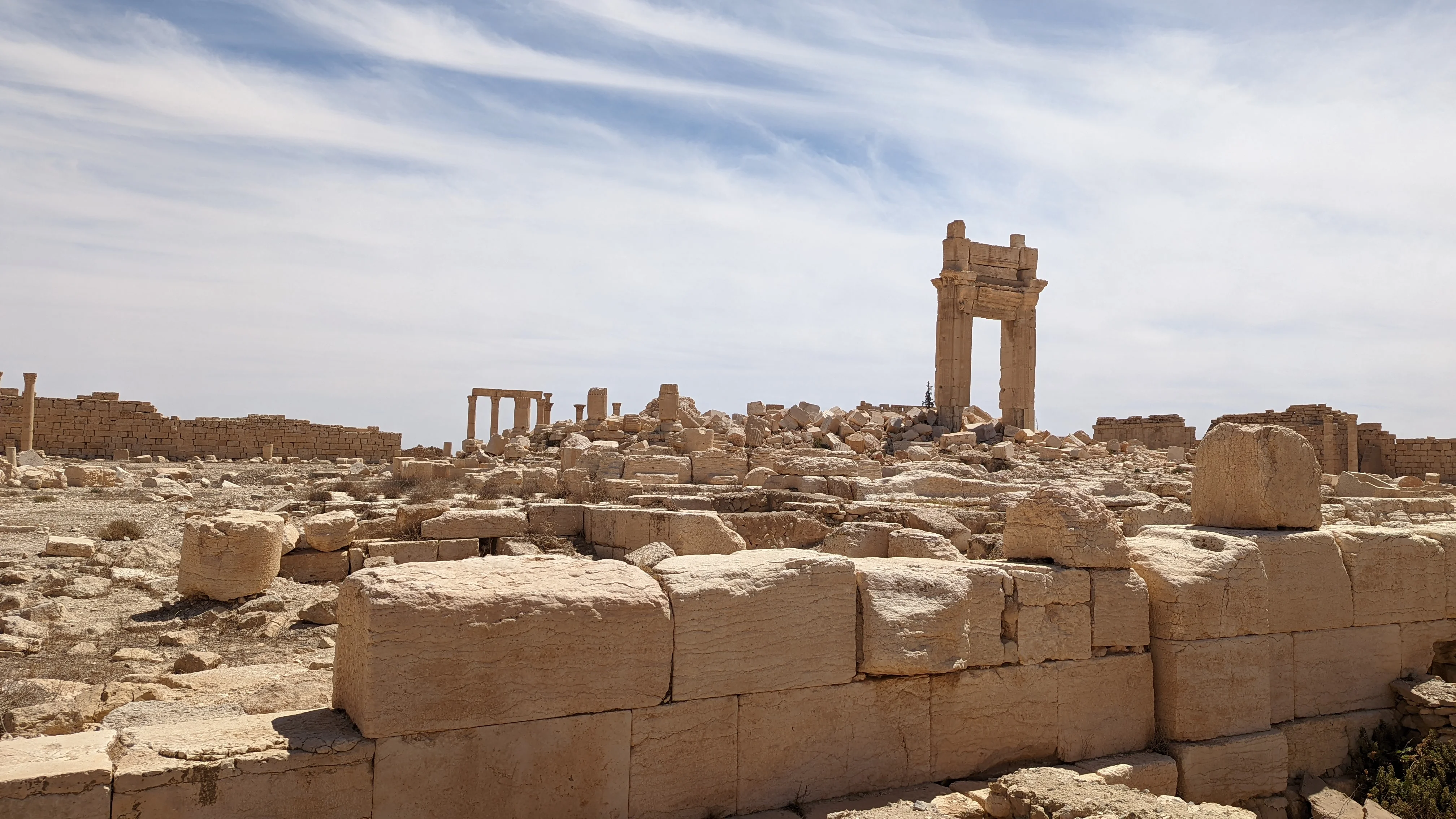 Rubble and partial columns from ancient Palmyra ruins scattered under a cloudy sky