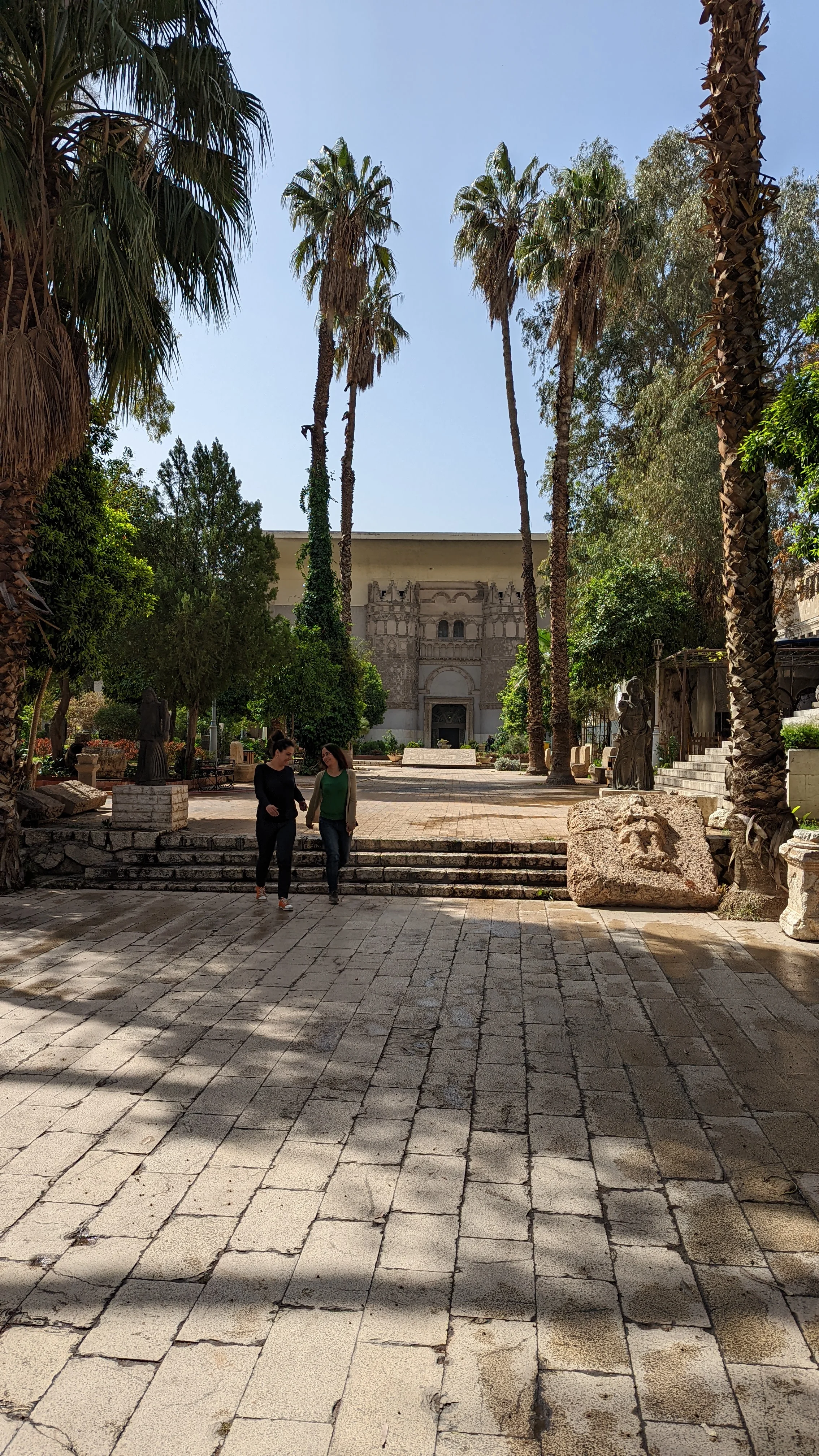 Entrance to the National Museum of Damascus framed by palm trees and stone statues
