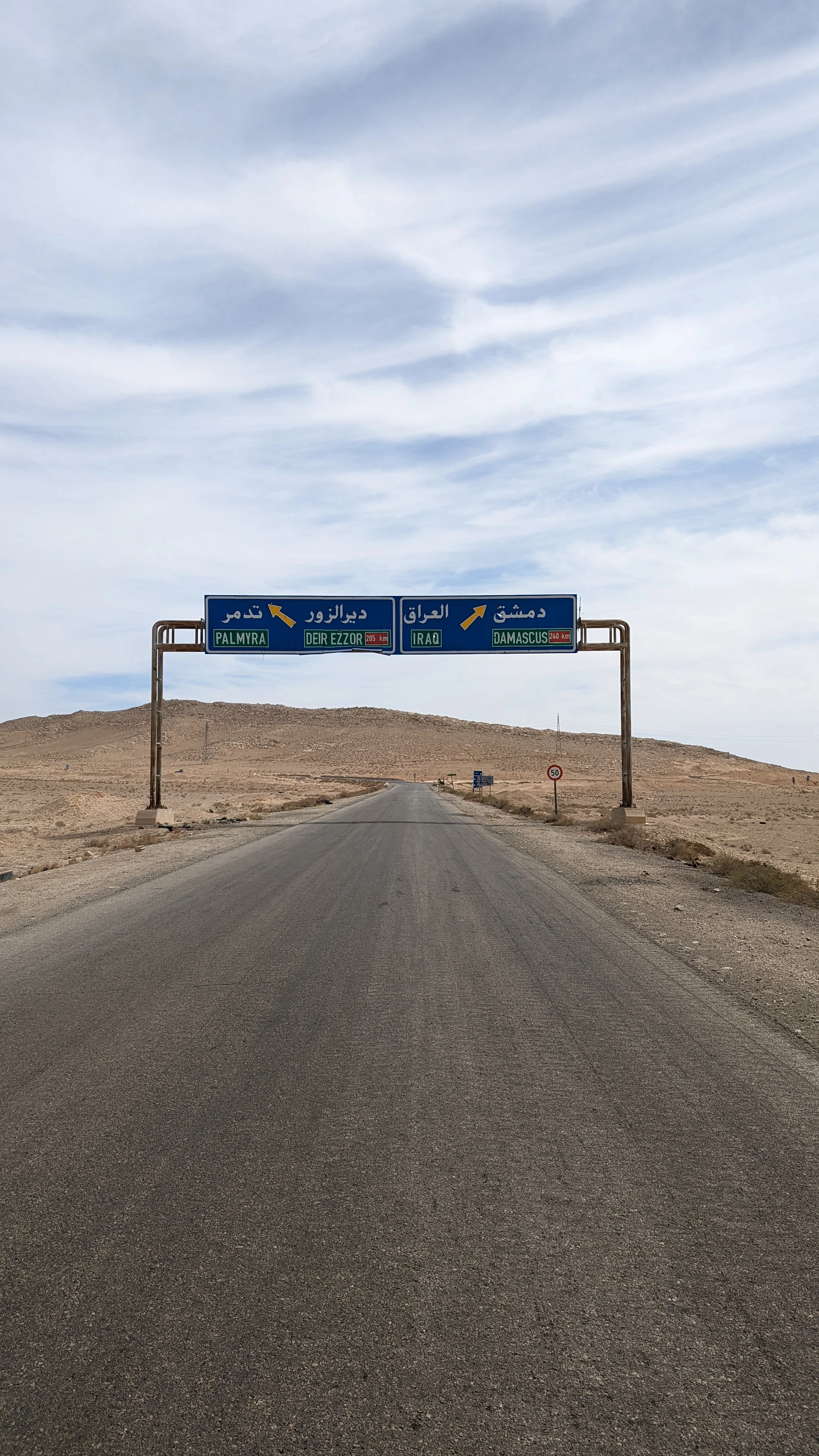 Road sign at Syria desert junction pointing to Palmyra, Deir Ezzor, Iraq, and Damascus