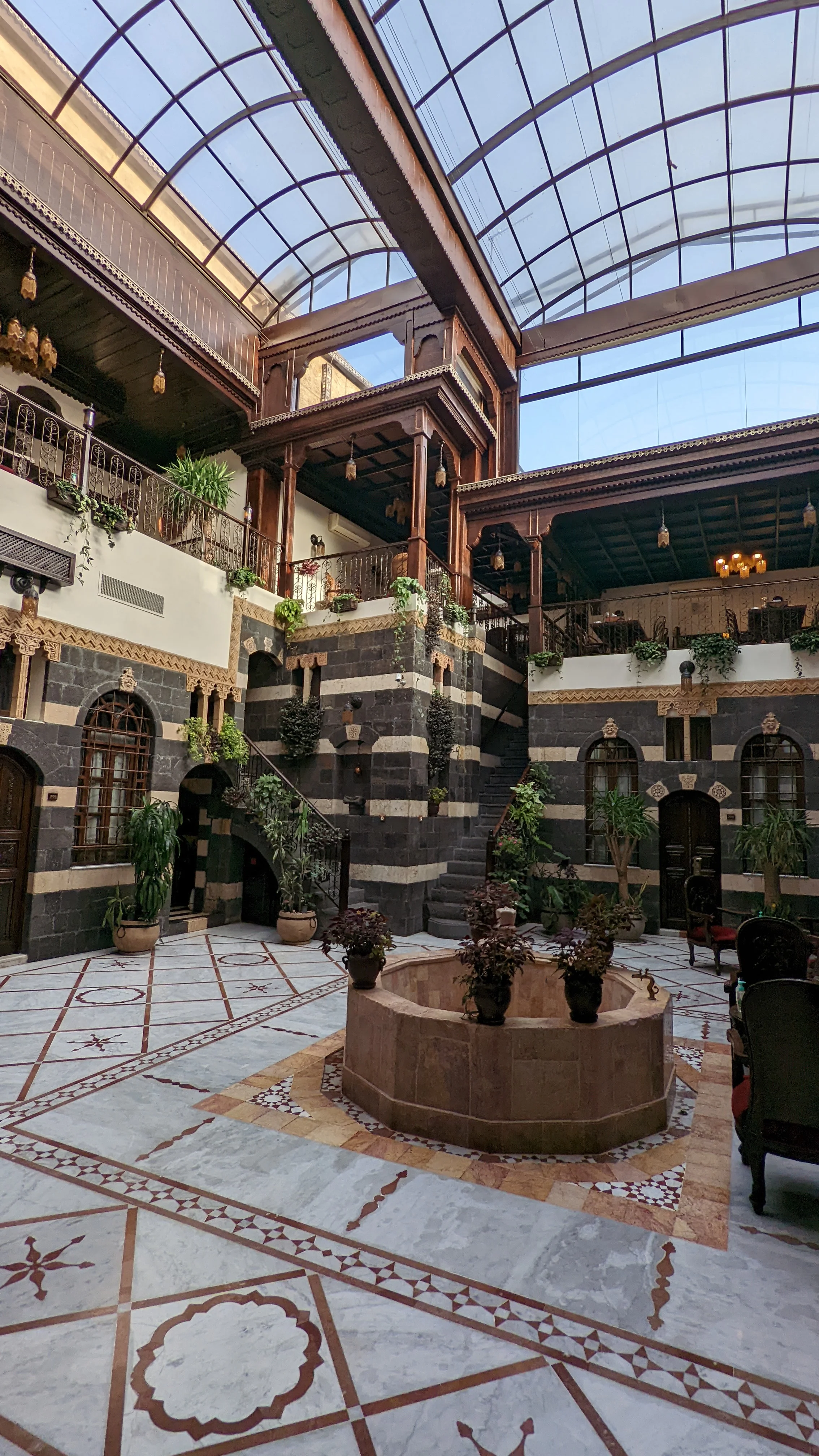 Traditional Damascene house courtyard with striped stone walls, indoor plants, and central fountain