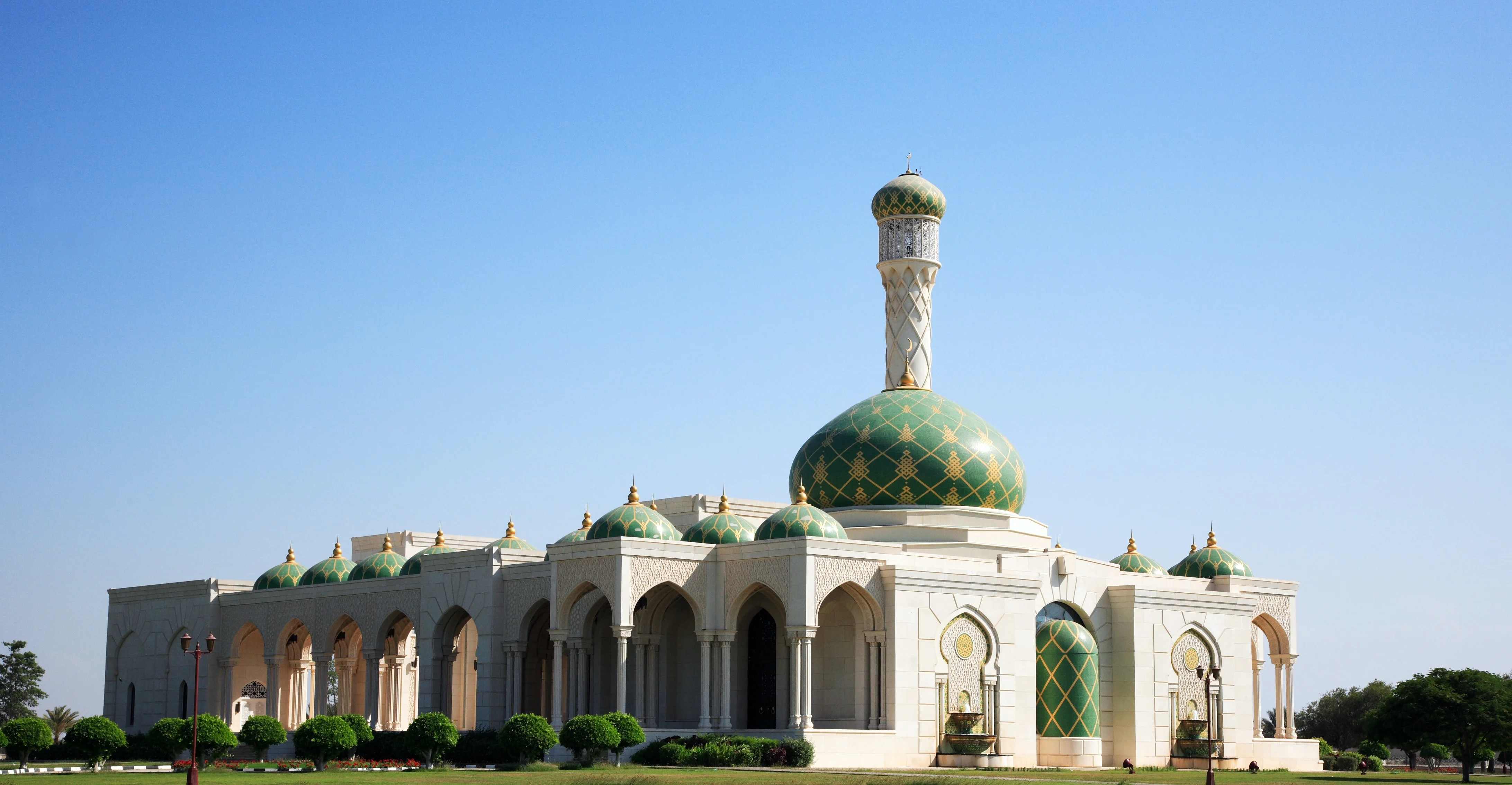 Grand mosque with green domes under blue sky, a key stop on an Oman tour.