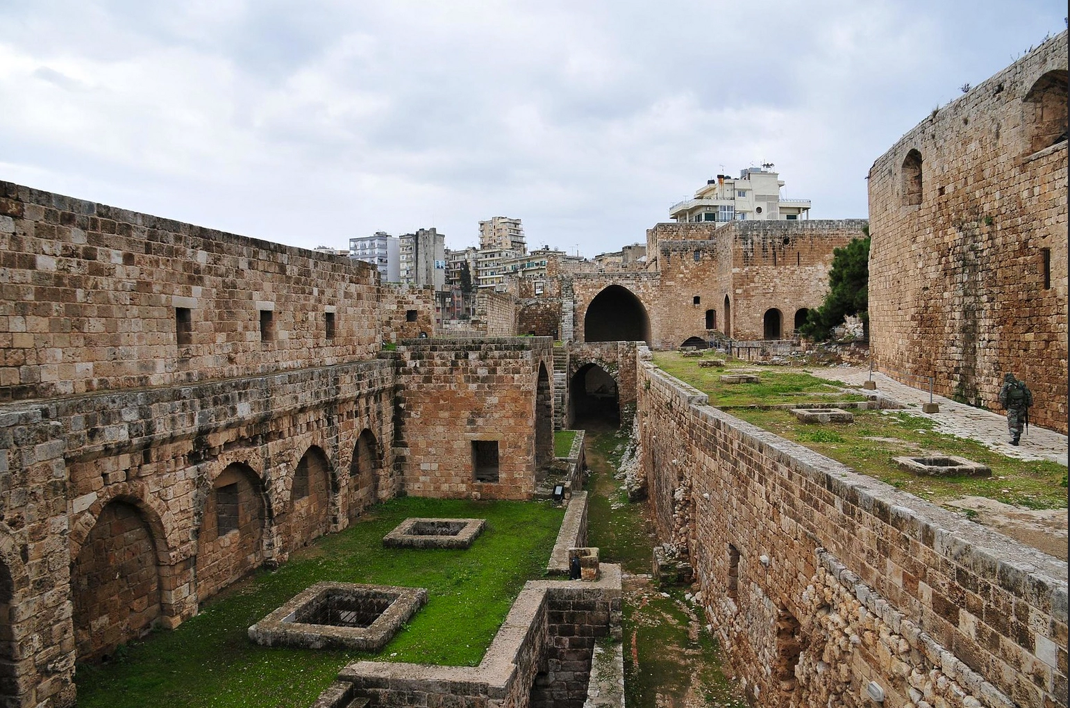 Old walls and inner courtyards of Tripoli Citadel with modern city buildings behind.