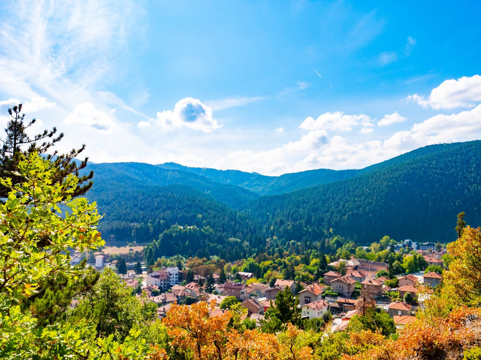 View over Bulgarian town surrounded by green mountains and blue sky in summer.