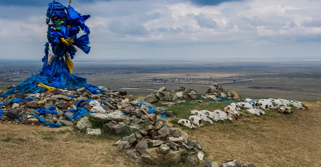 Ovoo cairn Mongolia, blue khadag ribbons and animal skulls on hill overlooking plains.