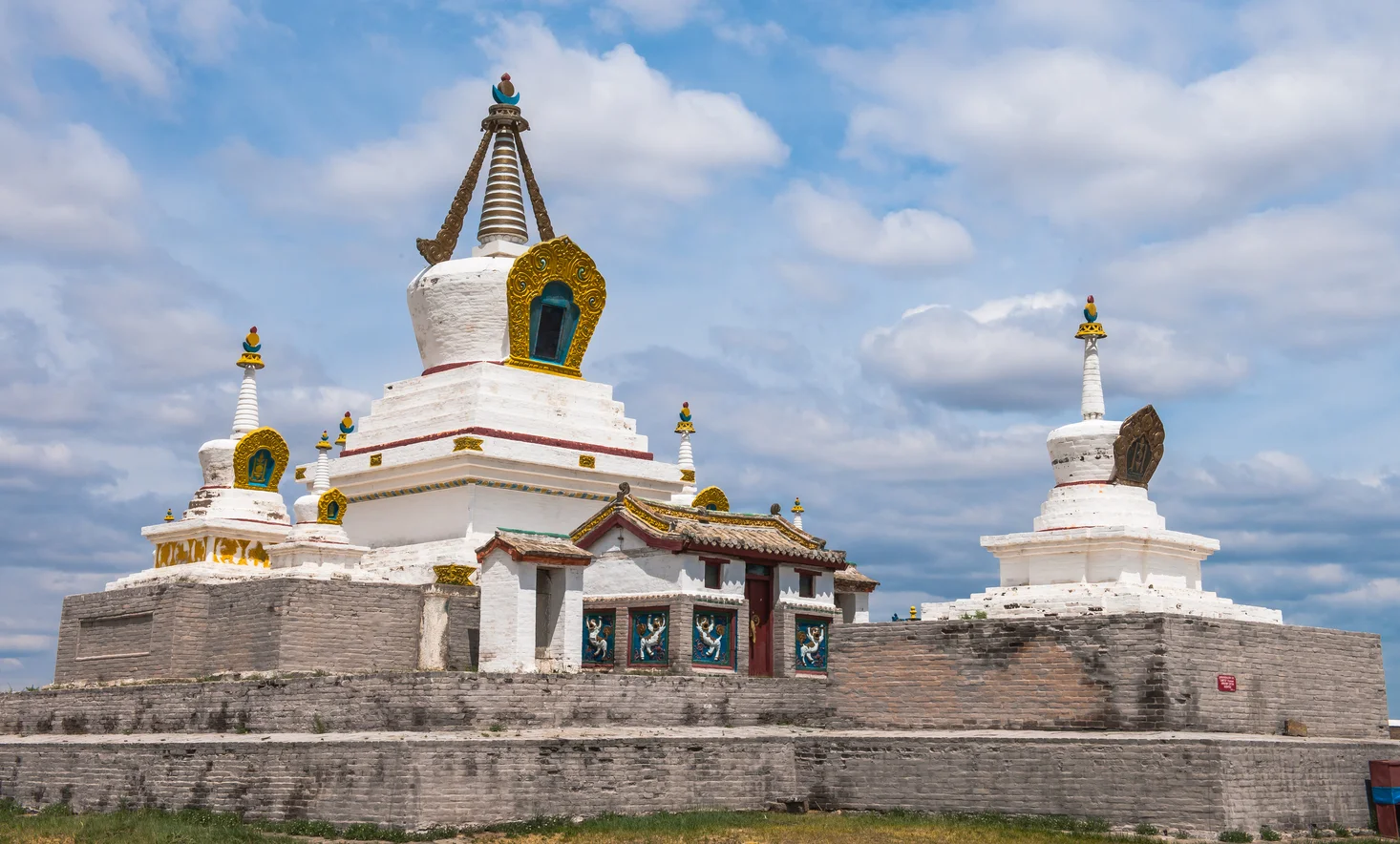 Erdenezuu Temple Mongolia, white stupas with gold trim under partly cloudy blue sky.