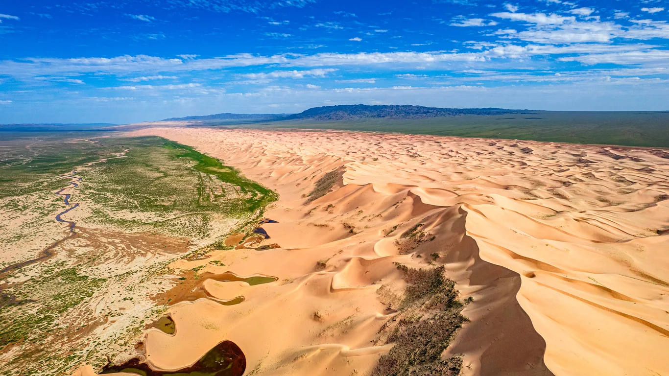 Khongoryn Els Mongolia, sweeping sand dunes beside lush green river valley.