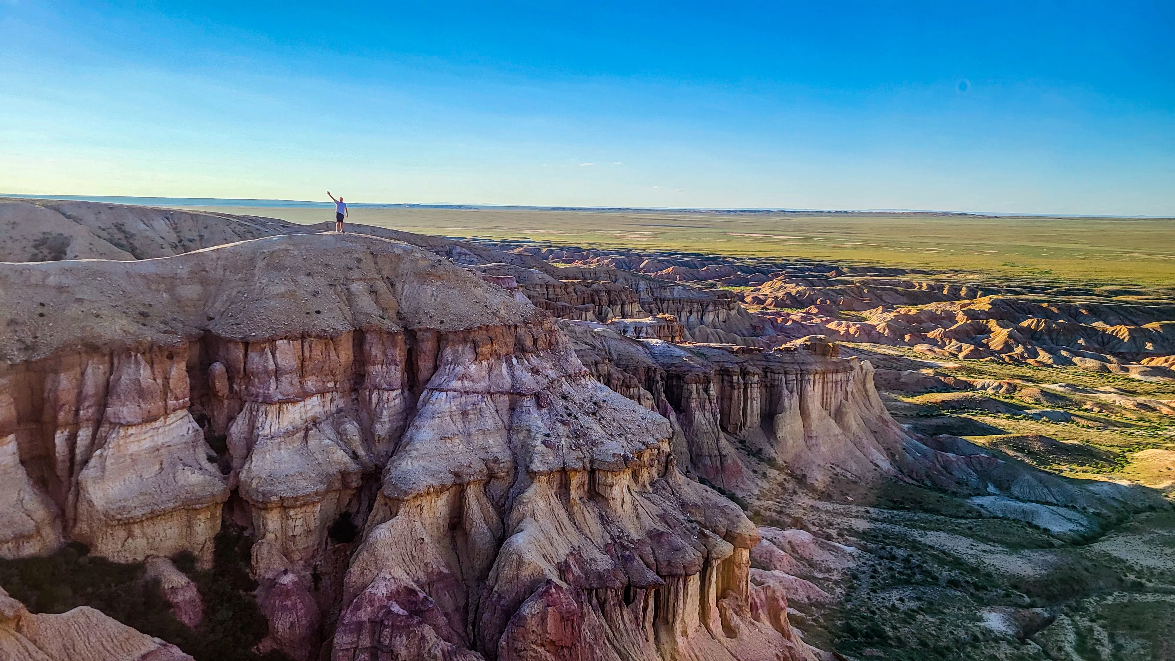 Man standing on Mongolia's colorful Flaming Cliffs with vast desert views.
