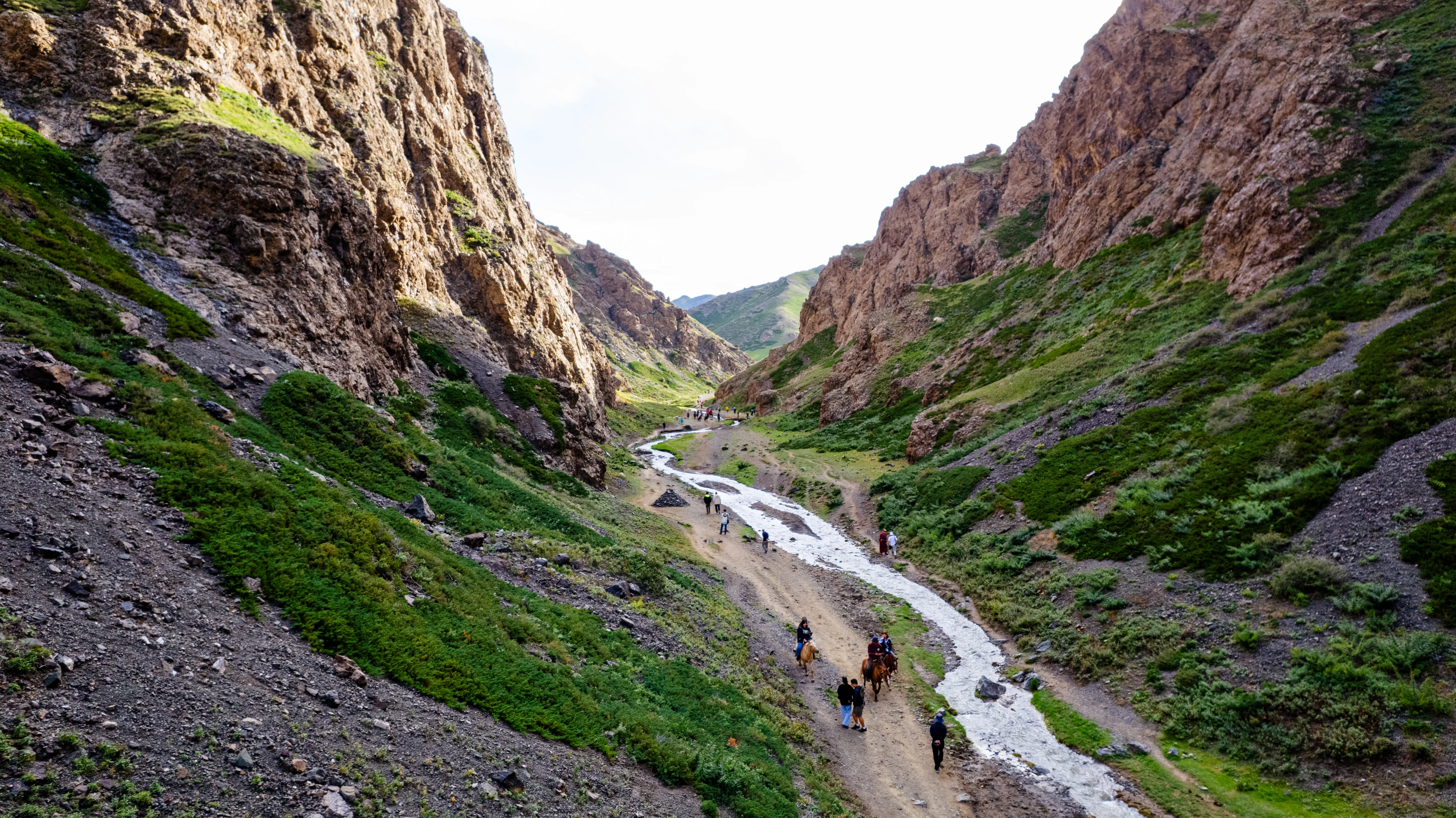 Tourists riding horses through Mongolia's Yol Valley between rocky cliffs.