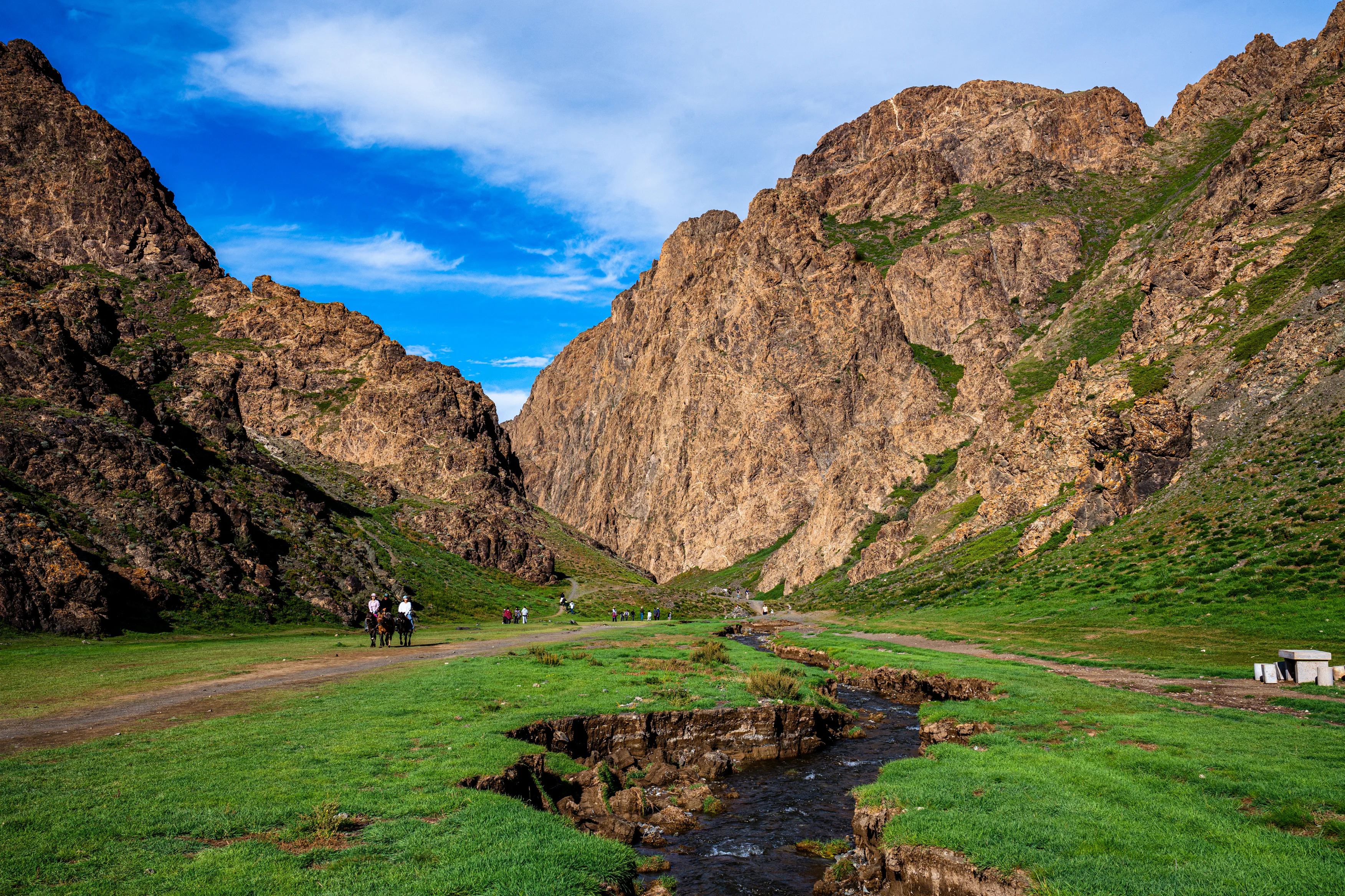 Yolyn Am gorge Mongolia with green valley, stream, brown cliffs and tourists on horseback.