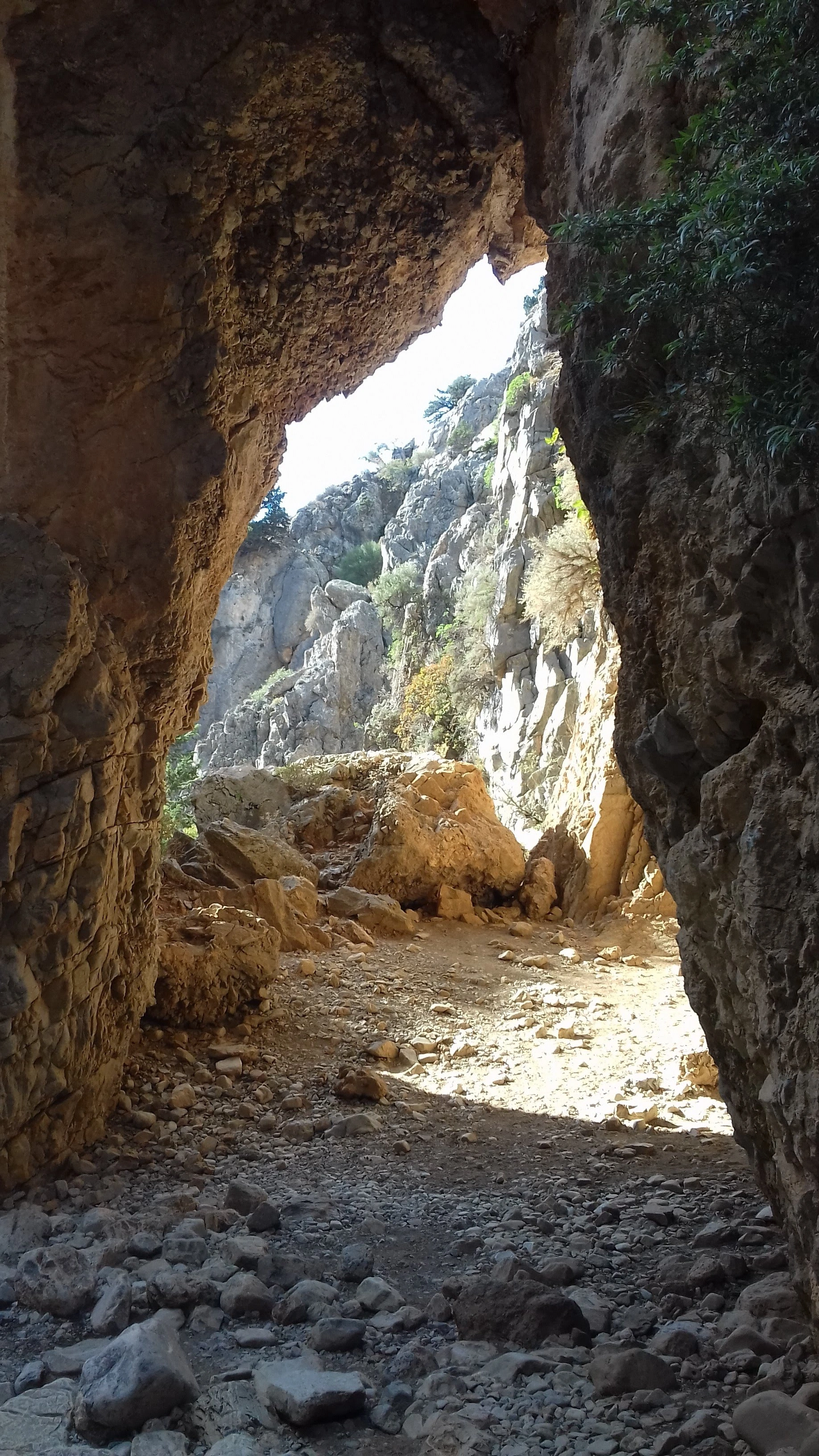Rocky path through a natural stone arch in a sunlit mountain gorge, Crete.