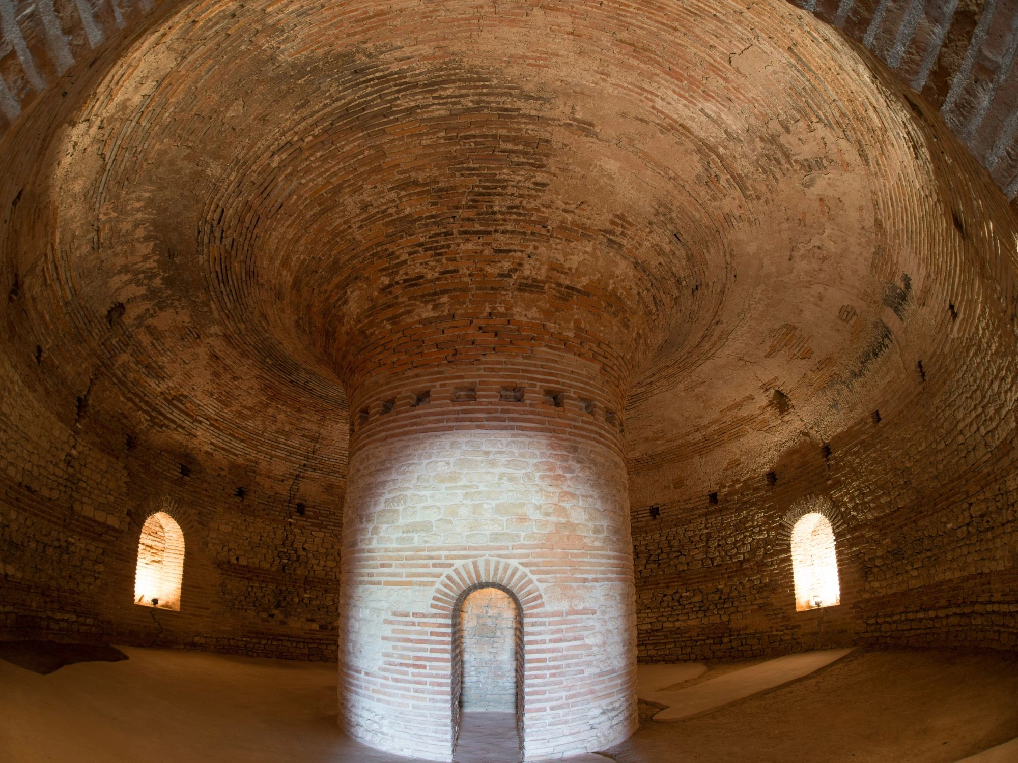 Interior of a round Thracian tomb with arched brick ceiling and narrow windows.