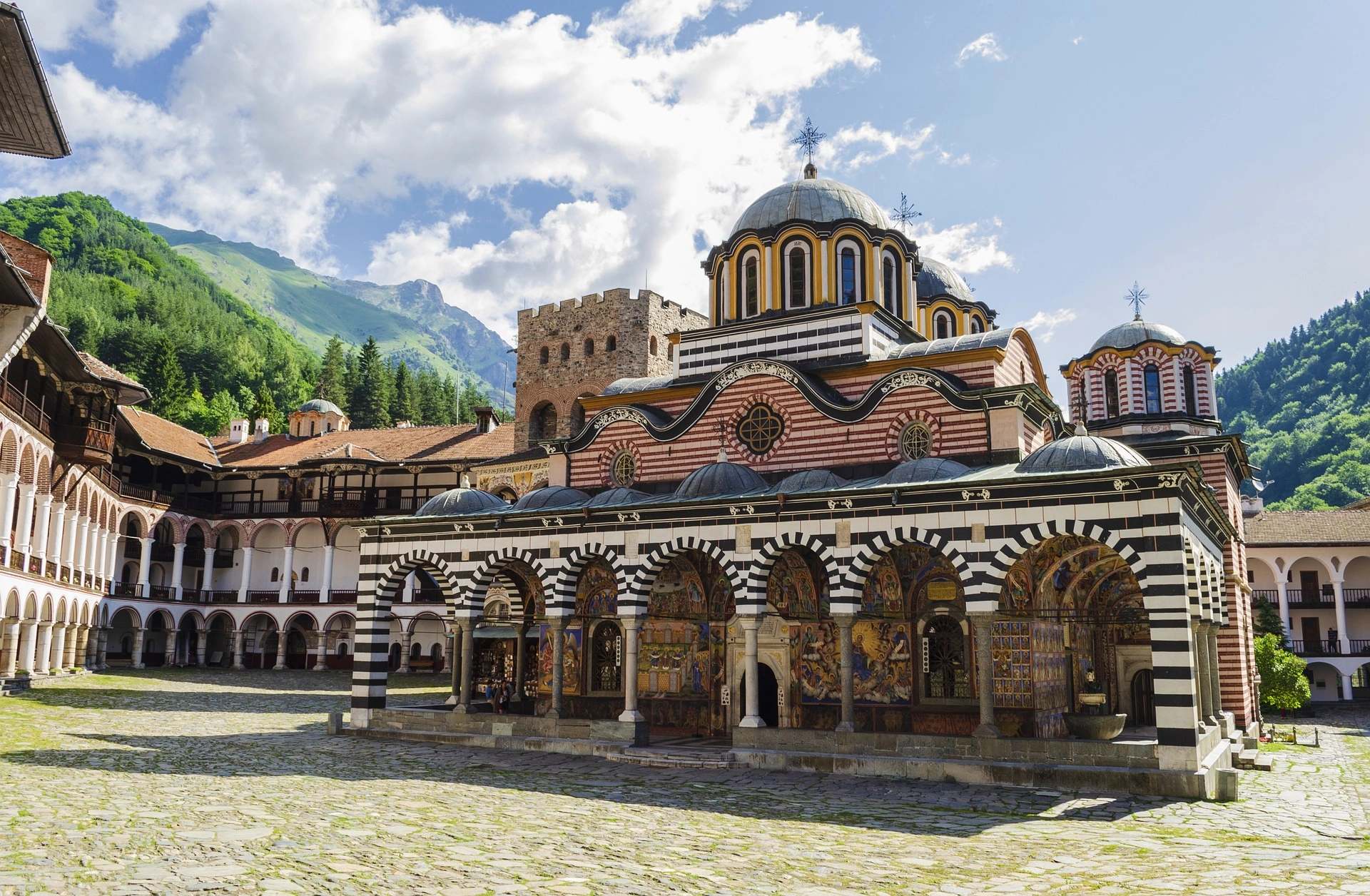 Exterior of Rila Monastery in Bulgaria with striped arches and mountain backdrop.