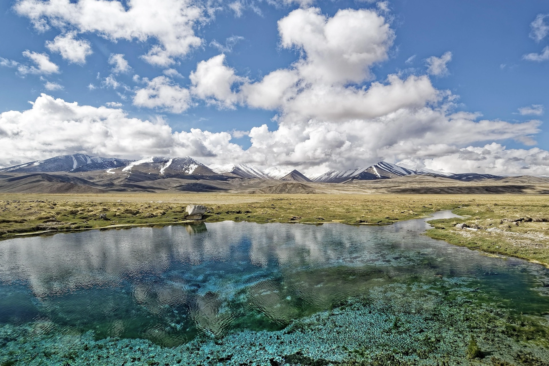 Crystal-clear alpine spring reflecting the Pamir Mountains under scattered clouds in Tajikistan.