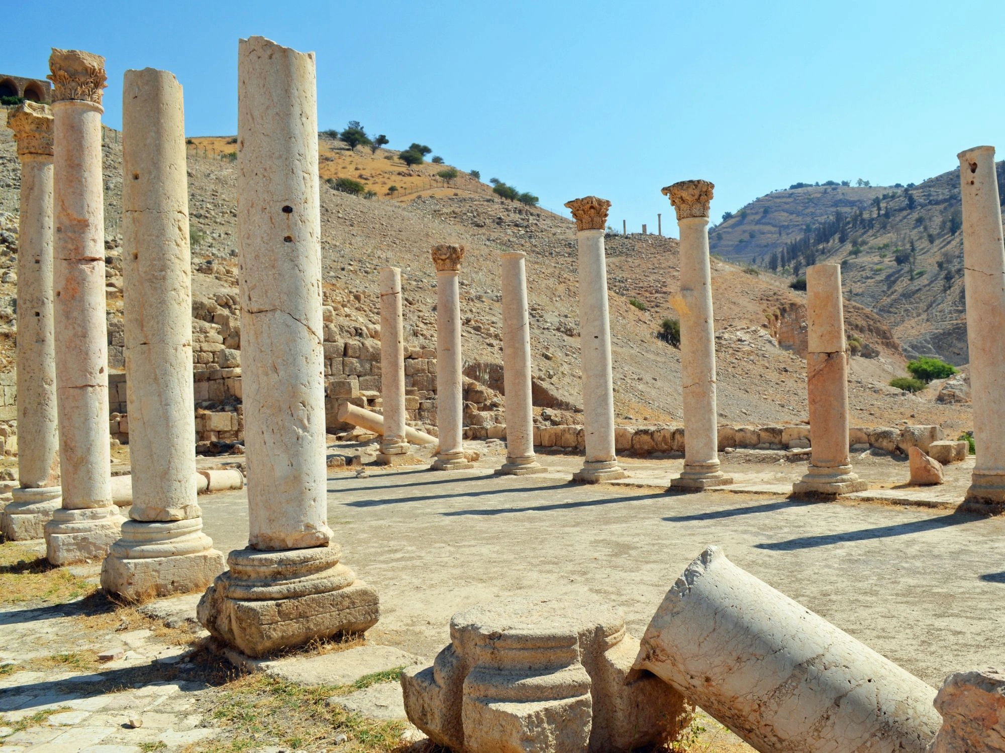 Ancient columns in Greece Pella site with stone ruins and hills under clear blue sky.