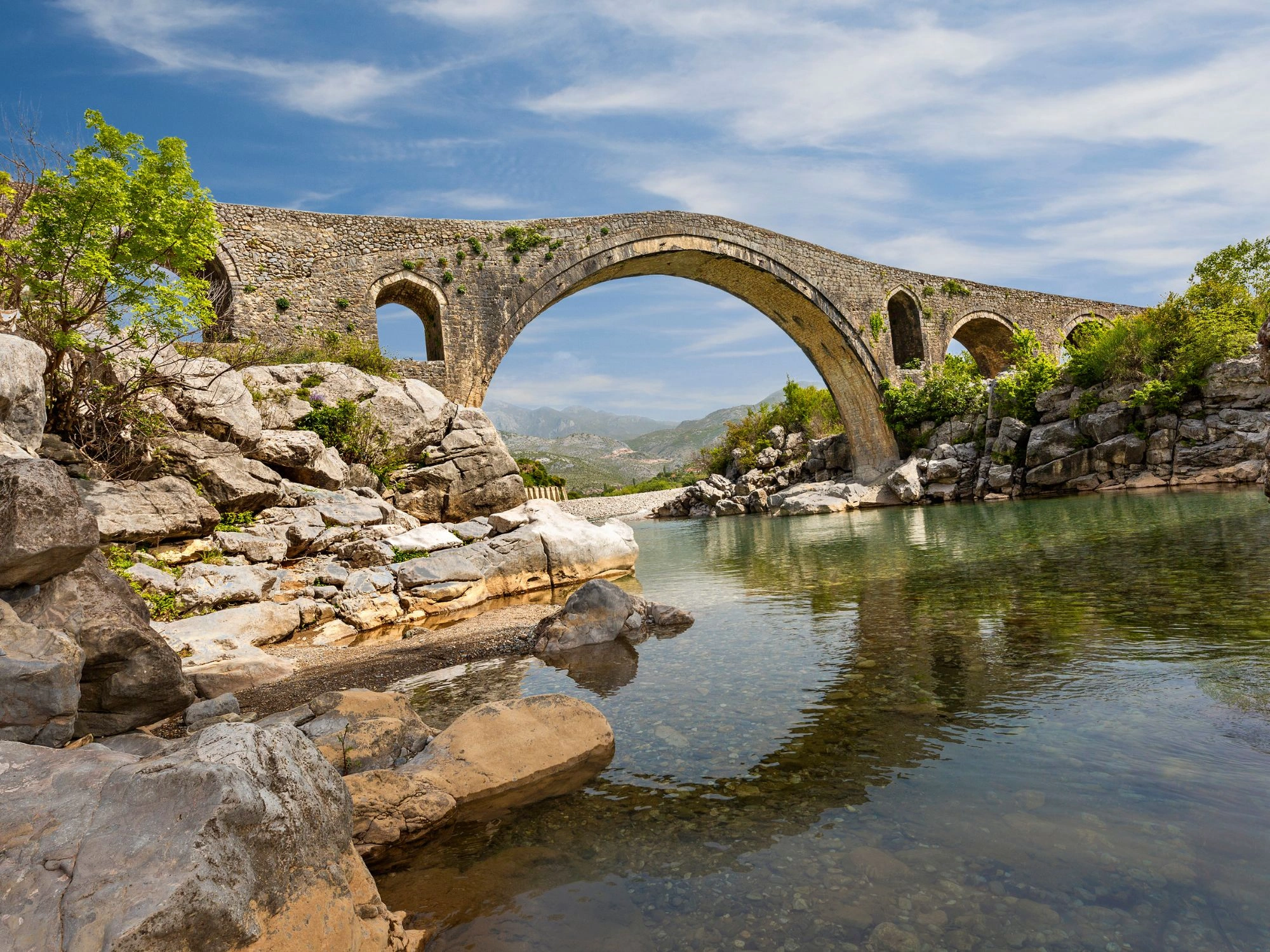 Stone arch bridge in Shkodër, Albania – iconic Ottoman-era architecture over calm river and rocks.