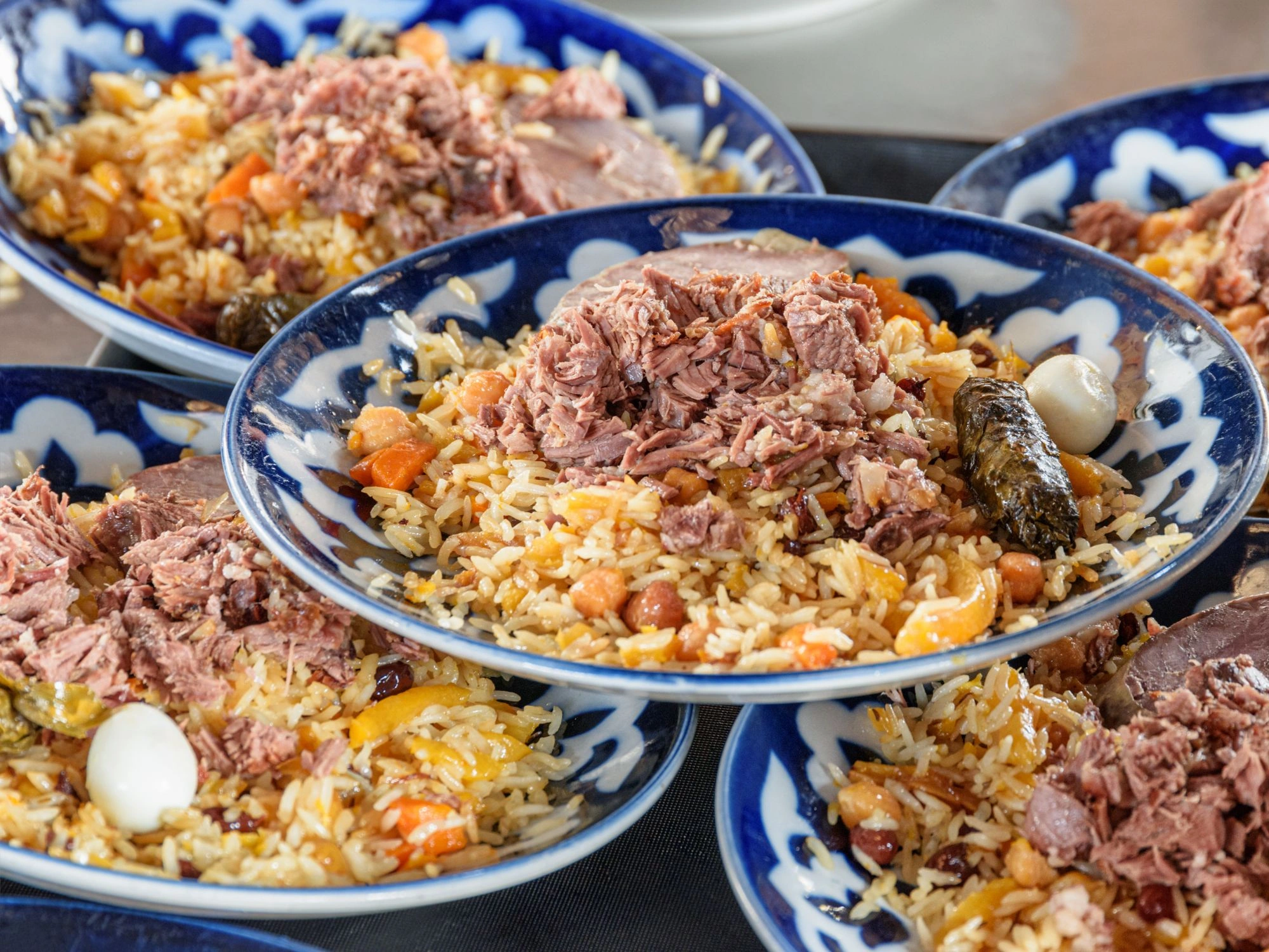 Traditional Uzbek plov with rice, lamb and vegetables served in blue ceramic bowls