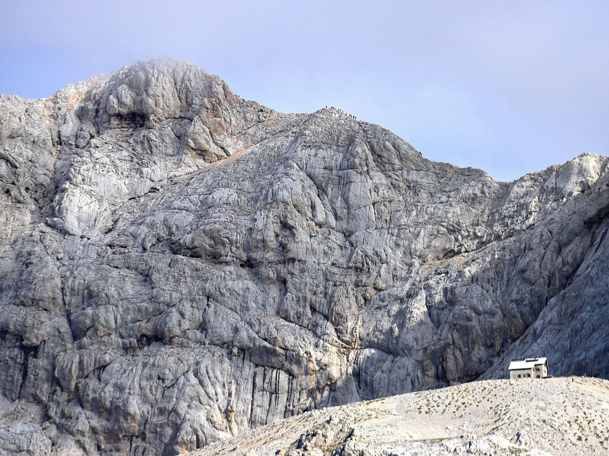 Rugged limestone summit of Mount Triglav with small mountain hut on barren slope, Slovenia