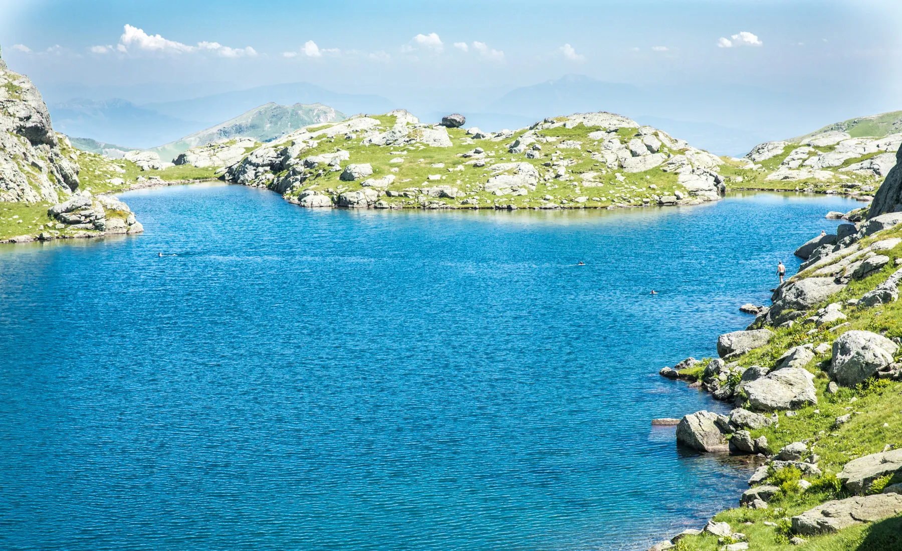 Clear blue waters of Gjeravica Lake, surrounded by grassy slopes and rocky outcrops in the Kosovo mountains