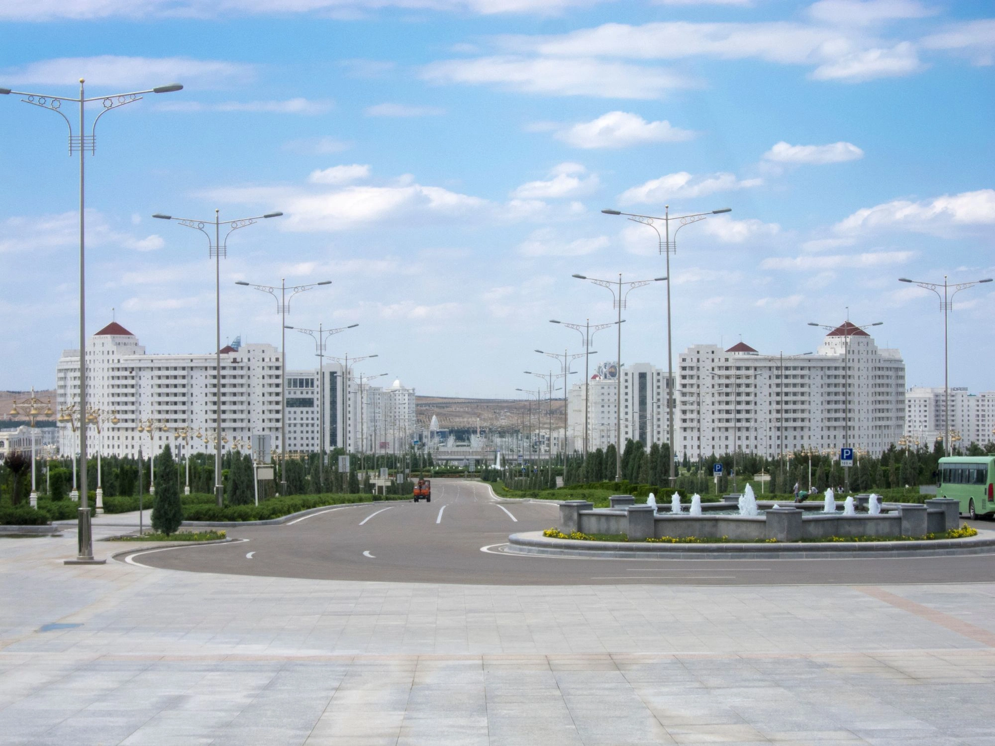 Modern buildings and landscaped boulevard in Ashgabat, Turkmenistan, under a blue sky.
