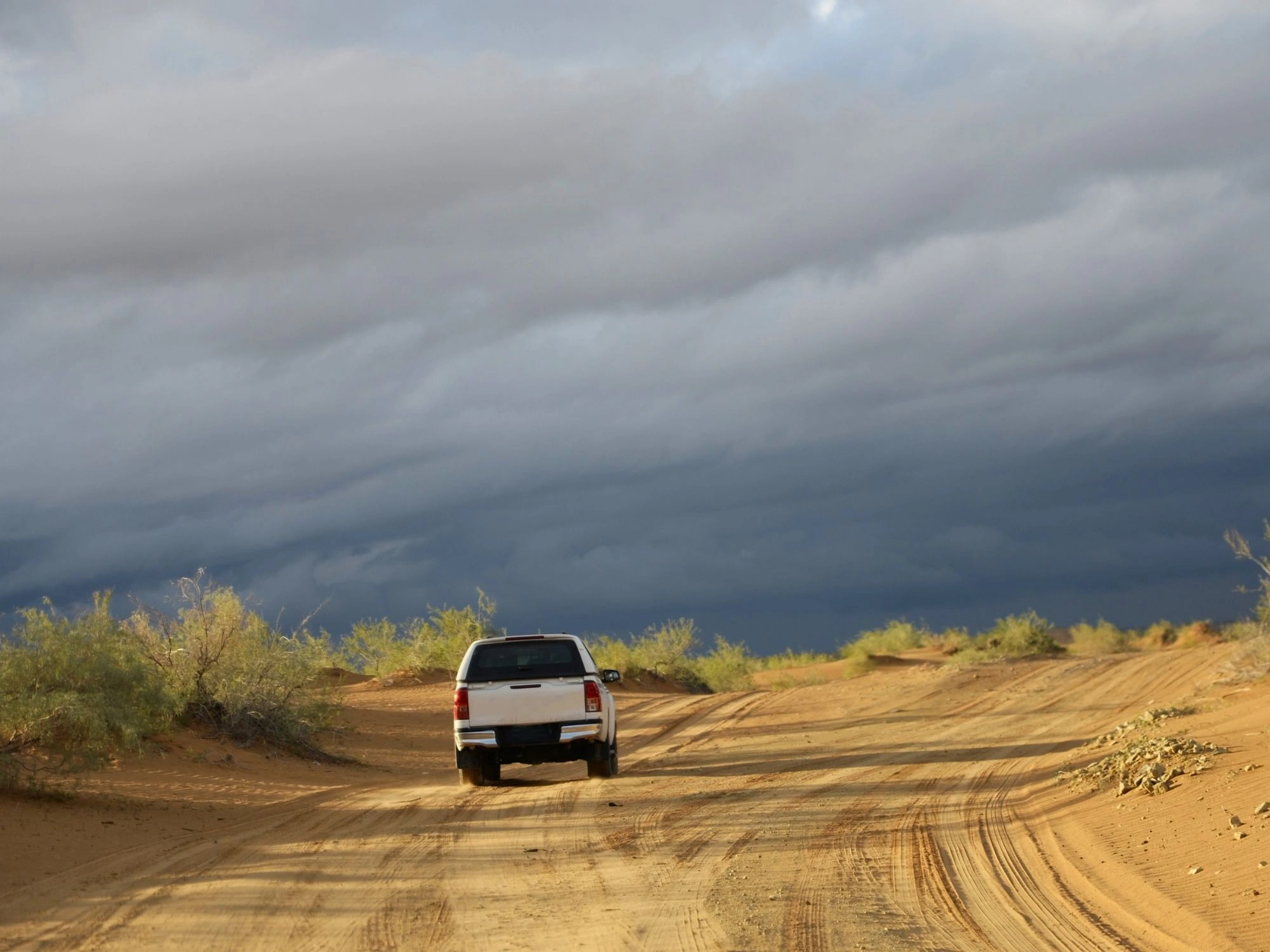 Off-road vehicle driving along sandy tracks in the Karakum Desert under storm clouds.
