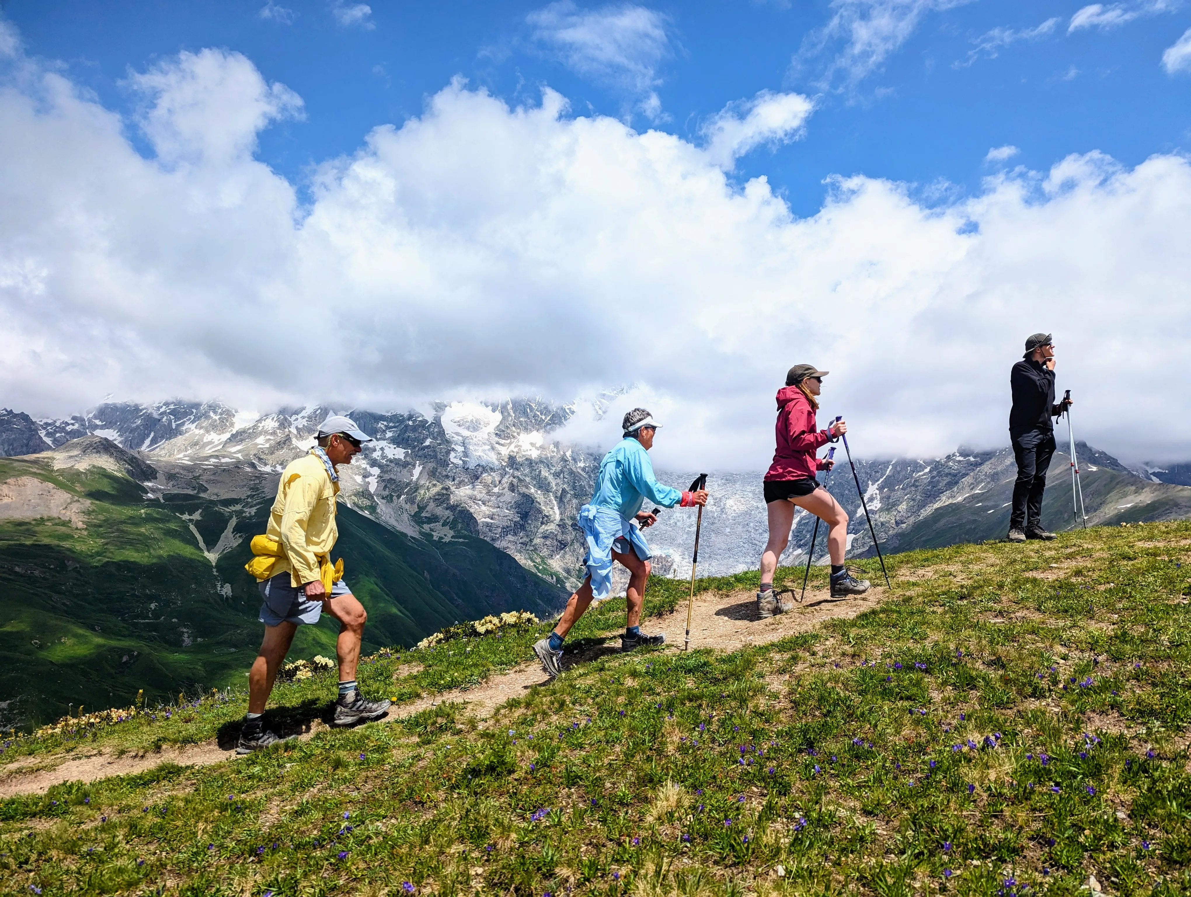 Hikers climbing grassy ridge with trekking poles against backdrop of snow-capped Caucasus mountains