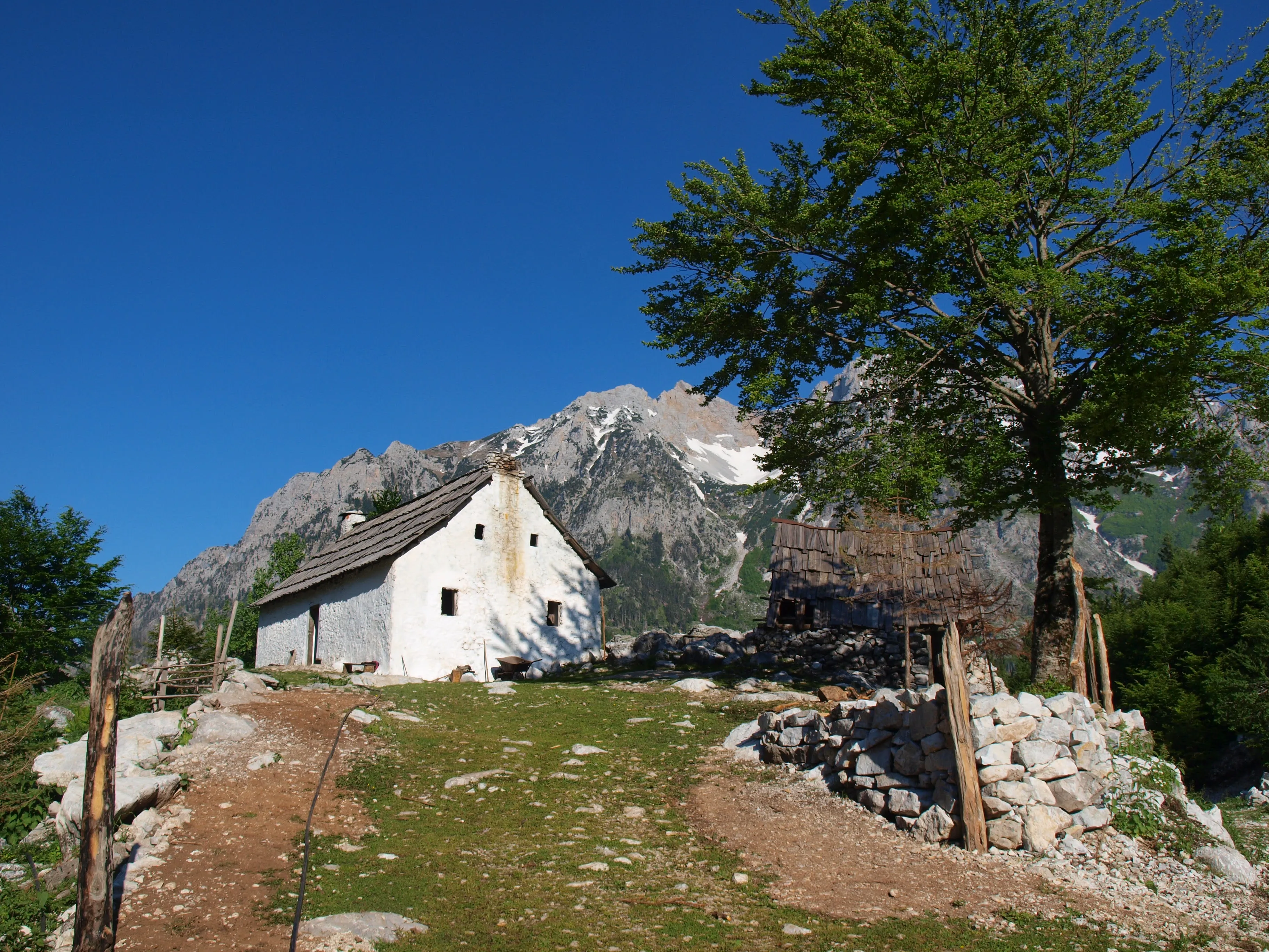 Traditional Albanian mountain hut in Valbona, surrounded by rocky terrain, greenery, and dramatic mountain views.