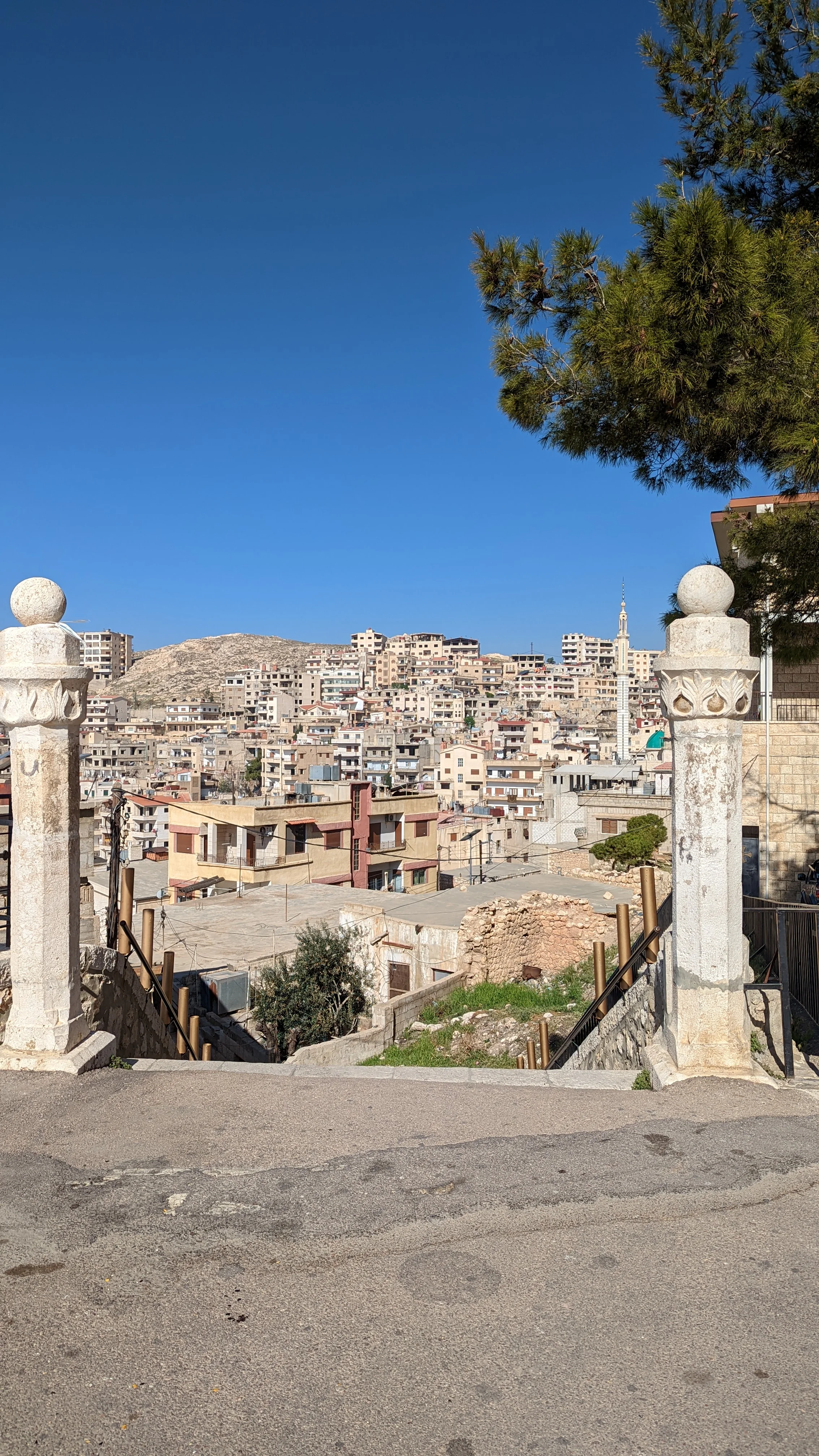 Hilltop view of Maaloula village with dense buildings and mosque minaret under a deep blue sky