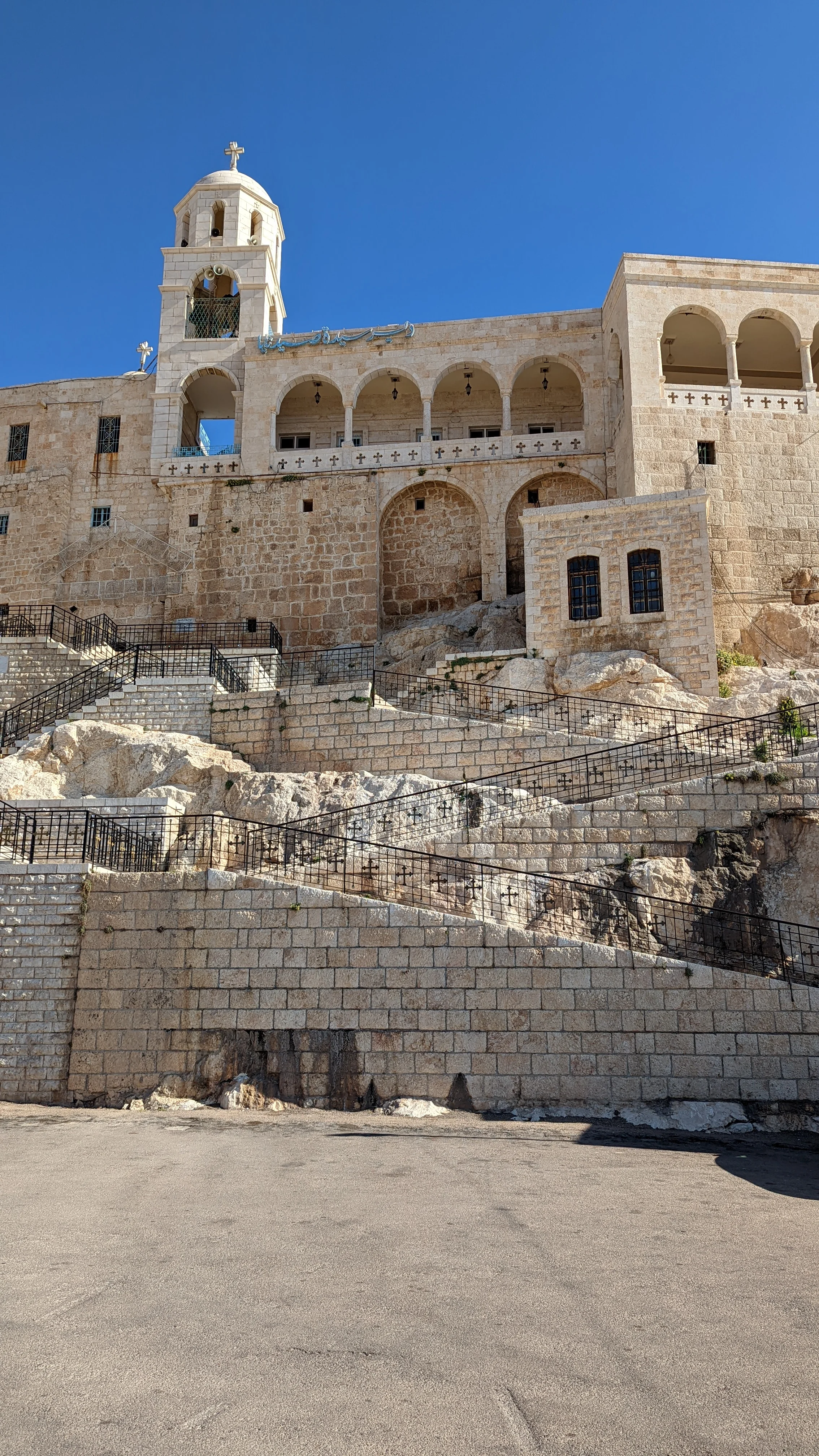 Exterior of Saint Thecla Monastery in Maaloula with stone arches, bell tower, and hillside steps