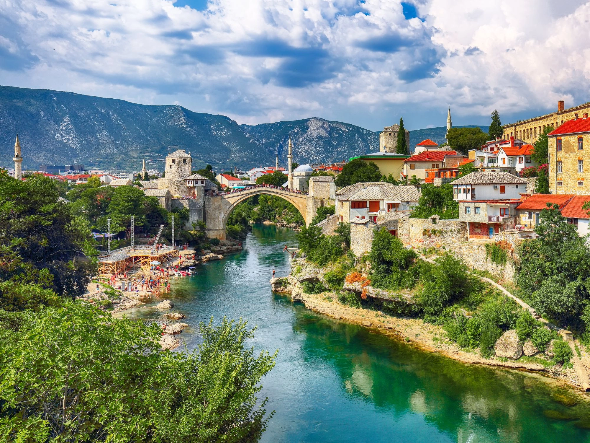 Mostar – Stari Most bridge in Bosnia with colorful buildings and people along the turquoise river.