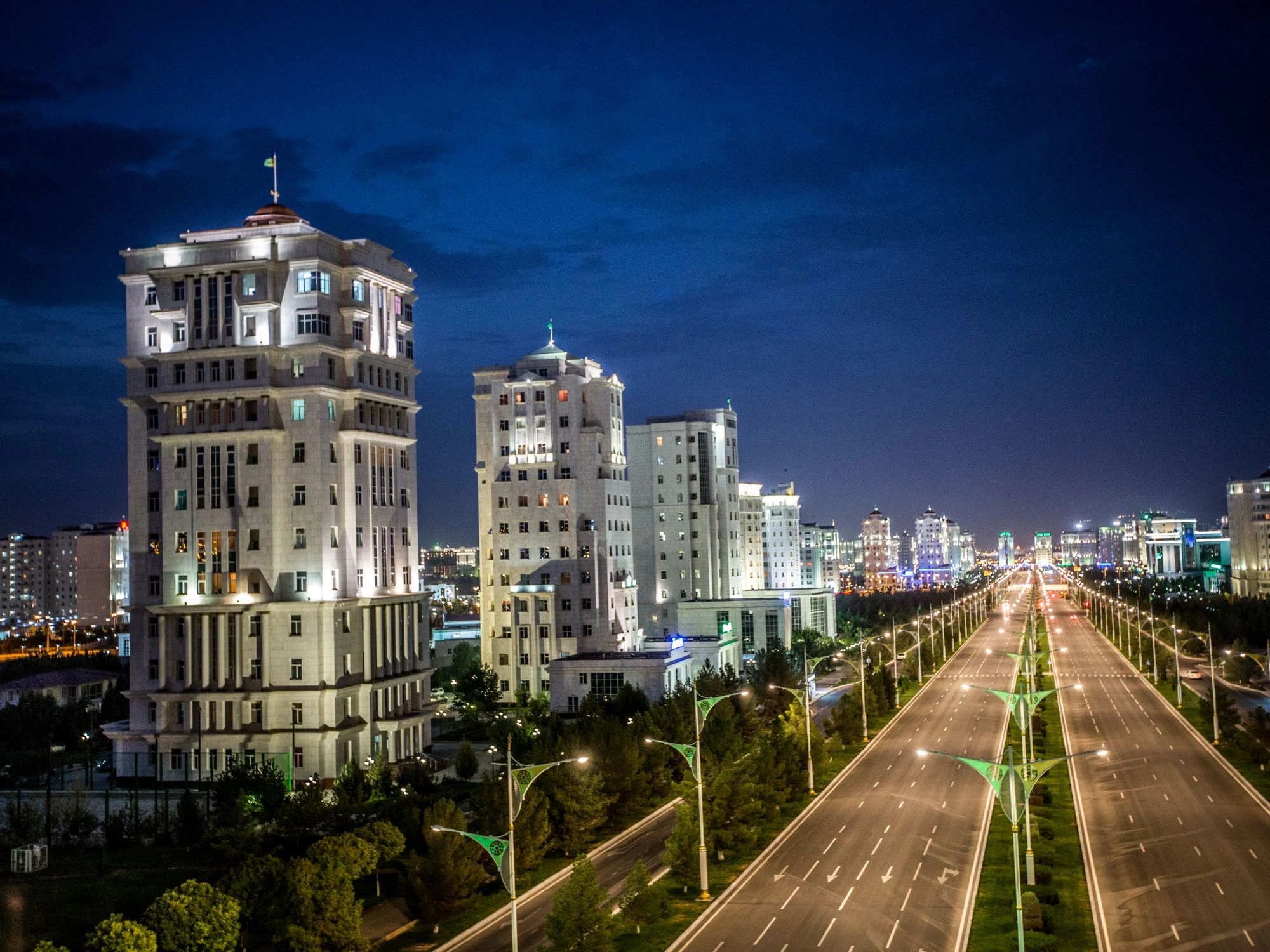Ashgabat skyline at night with illuminated white marble buildings and a wide avenue.