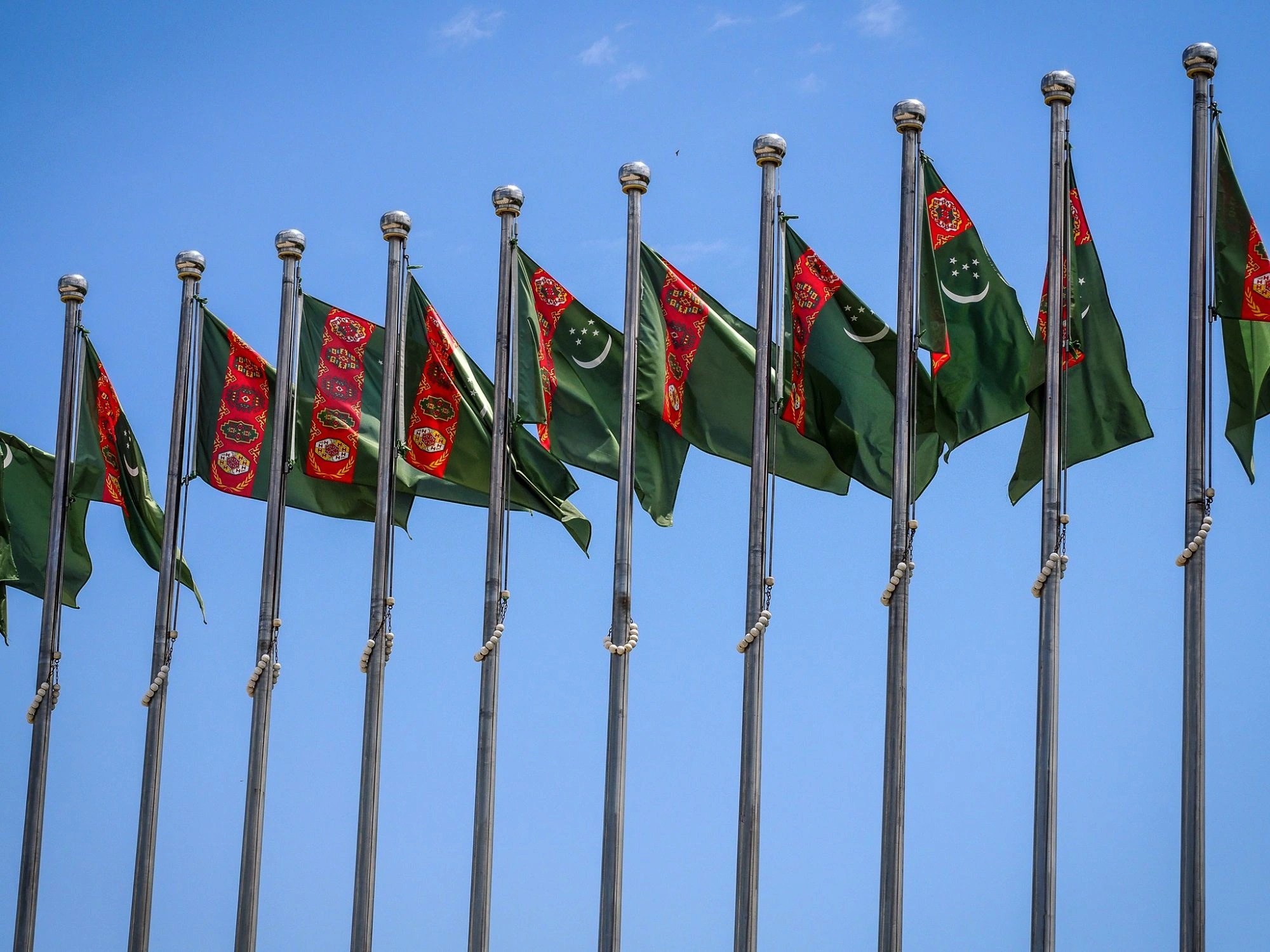Row of green Turkmenistan flags fluttering against a bright blue sky.