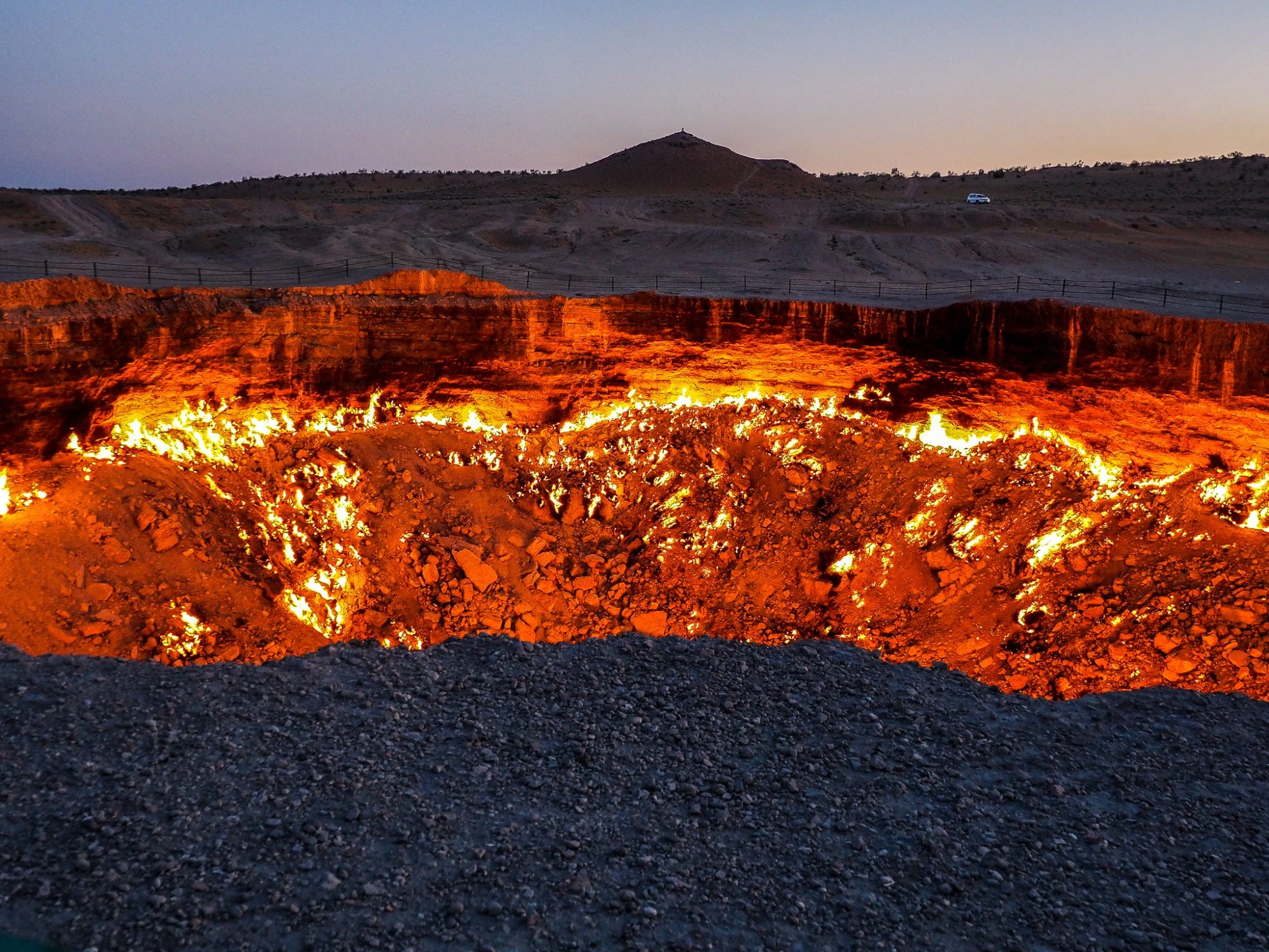 Fiery Darvaza Gas Crater in Turkmenistan, glowing at twilight with a dramatic sky.
