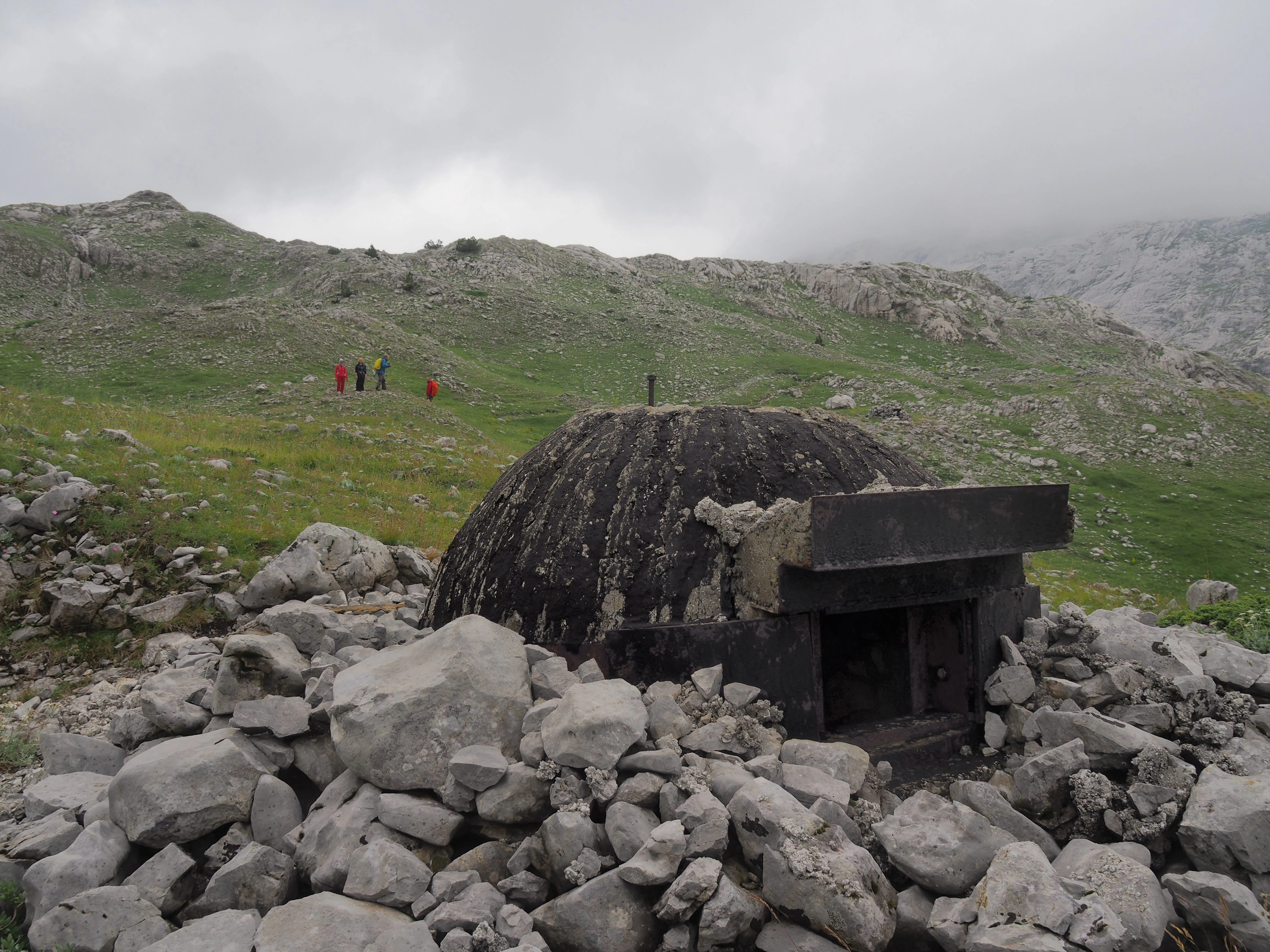 An abandoned concrete bunker, partially buried in rocky terrain, with misty mountain peaks in the background.